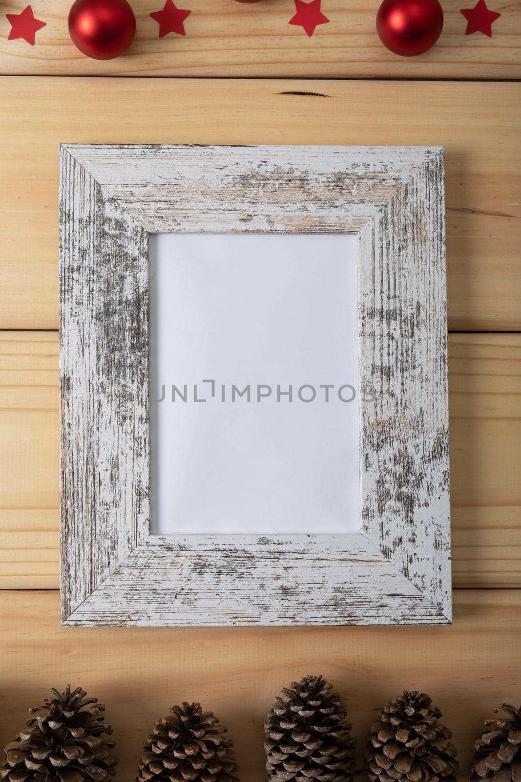 Composition of white card in frame with copy space, pine cones and baubles on wooden background. christmas, tradition and celebration concept.