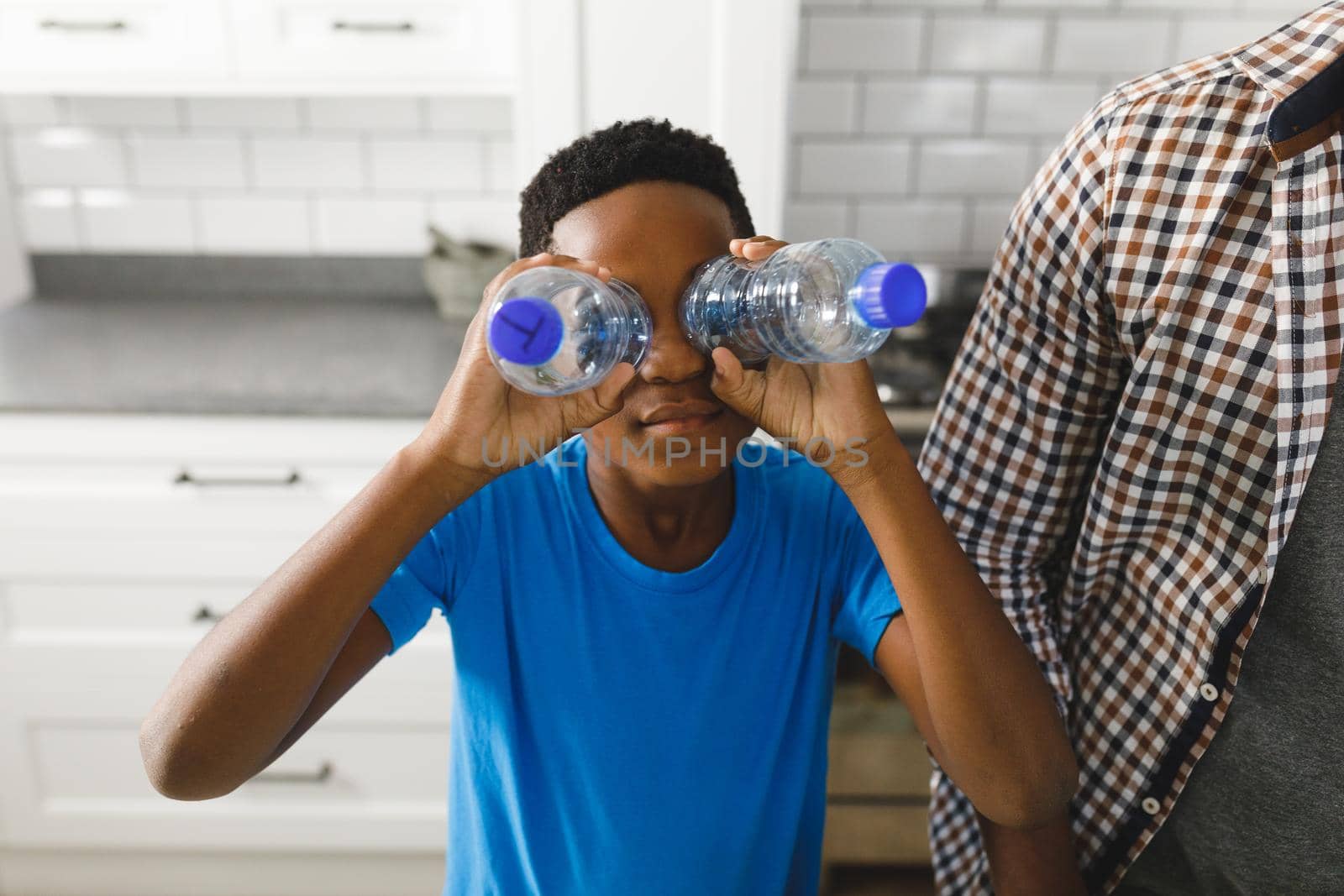 Happy african american son sorting recycling with father in kitchen, playing with plastic bottles by Wavebreakmedia