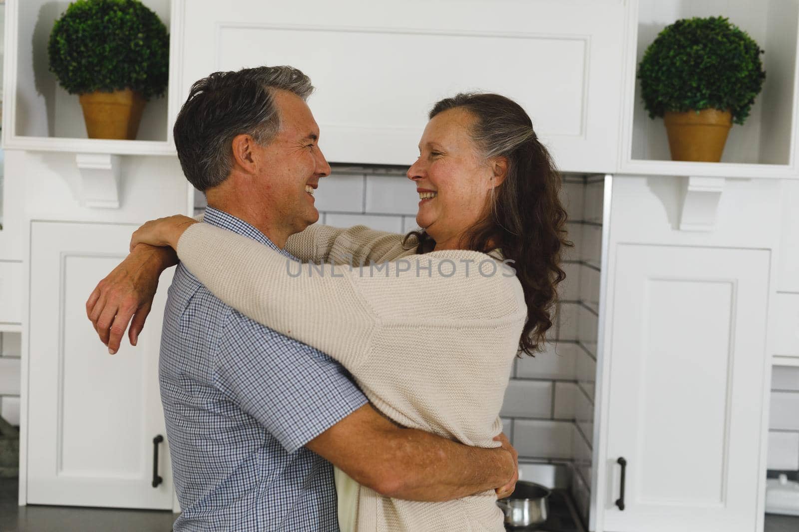 Happy senior caucasian couple in modern kitchen, embracing and smiling. retirement lifestyle, spending time at home.