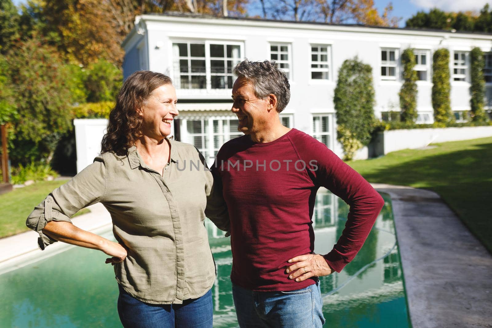 Happy senior caucasian couple embracing and smiling in sunny garden. luxury retirement lifestyle, spending time at home.