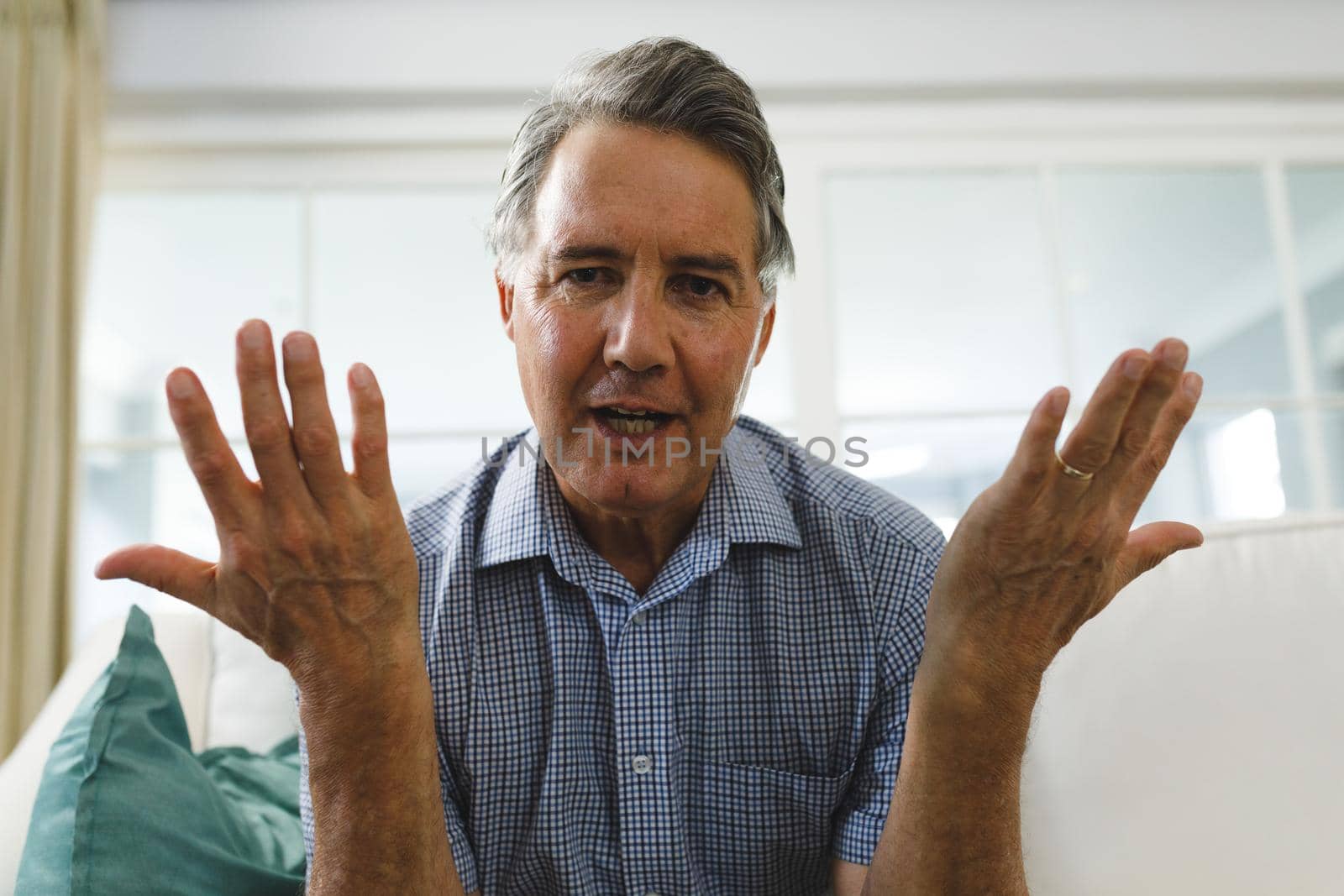 Senior caucasian man in living room, sitting on sofa, gesturing and talking during video call. retirement lifestyle, spending time at home with technology.