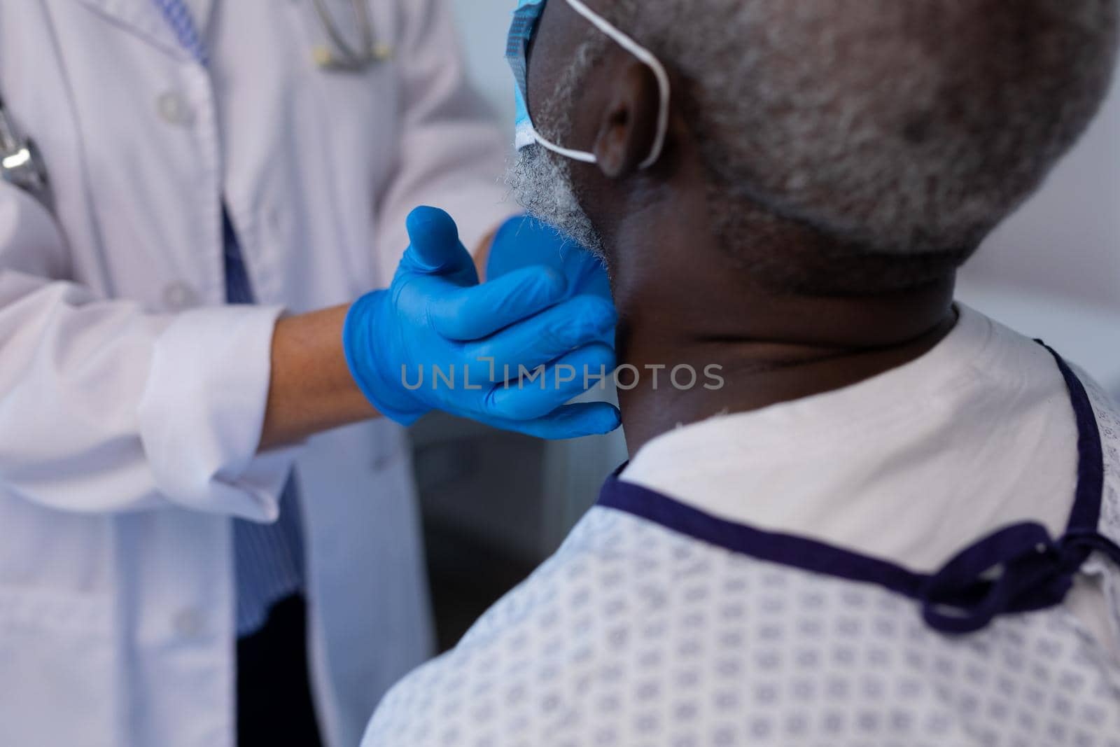 Caucasian female doctor palpating lymph nodes of african american male patient wearing mask. medicine, health and healthcare services during coronavirus covid 19 pandemic.