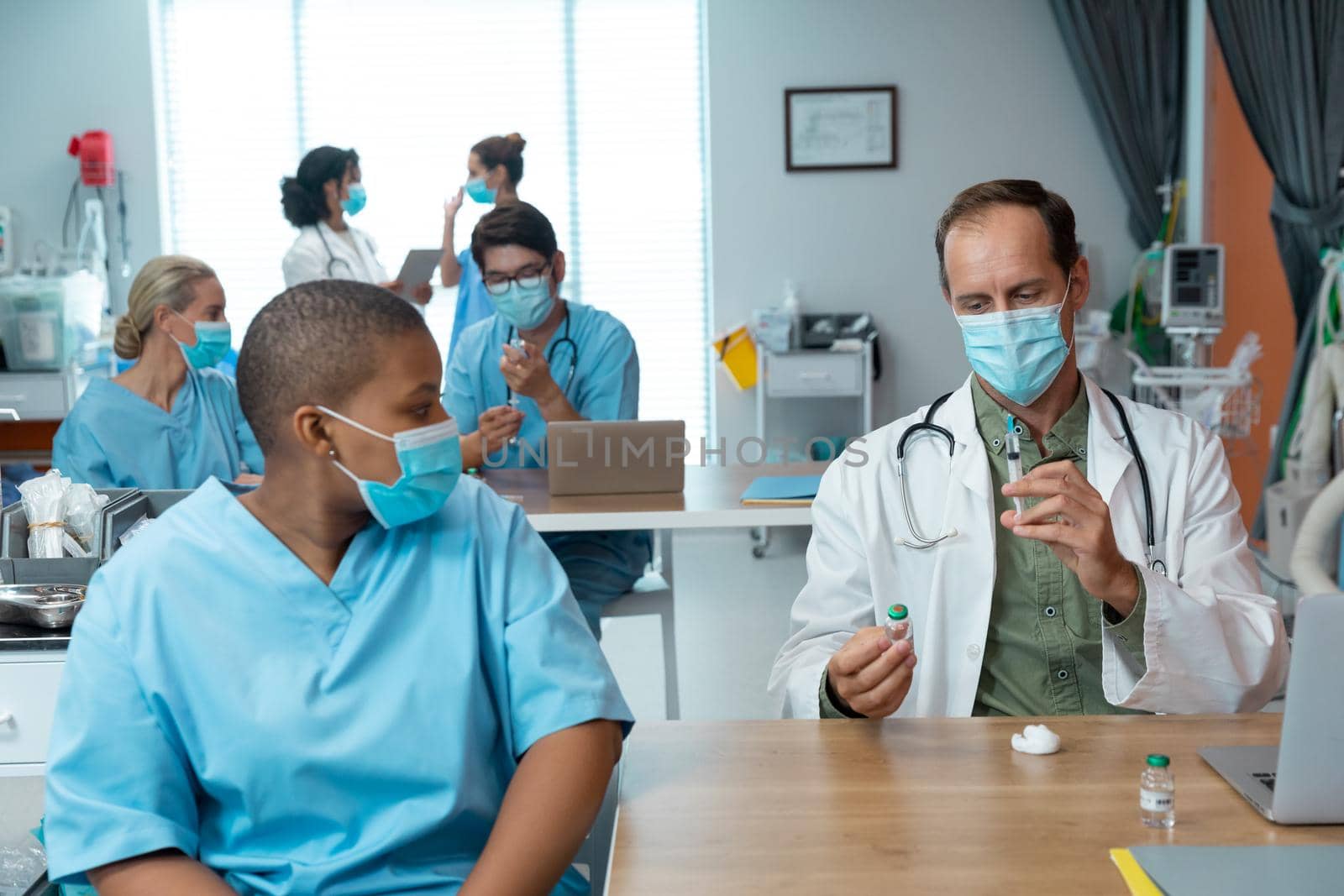 Caucasian male doctor in face mask preparing covid vaccination for female colleague in hospital by Wavebreakmedia