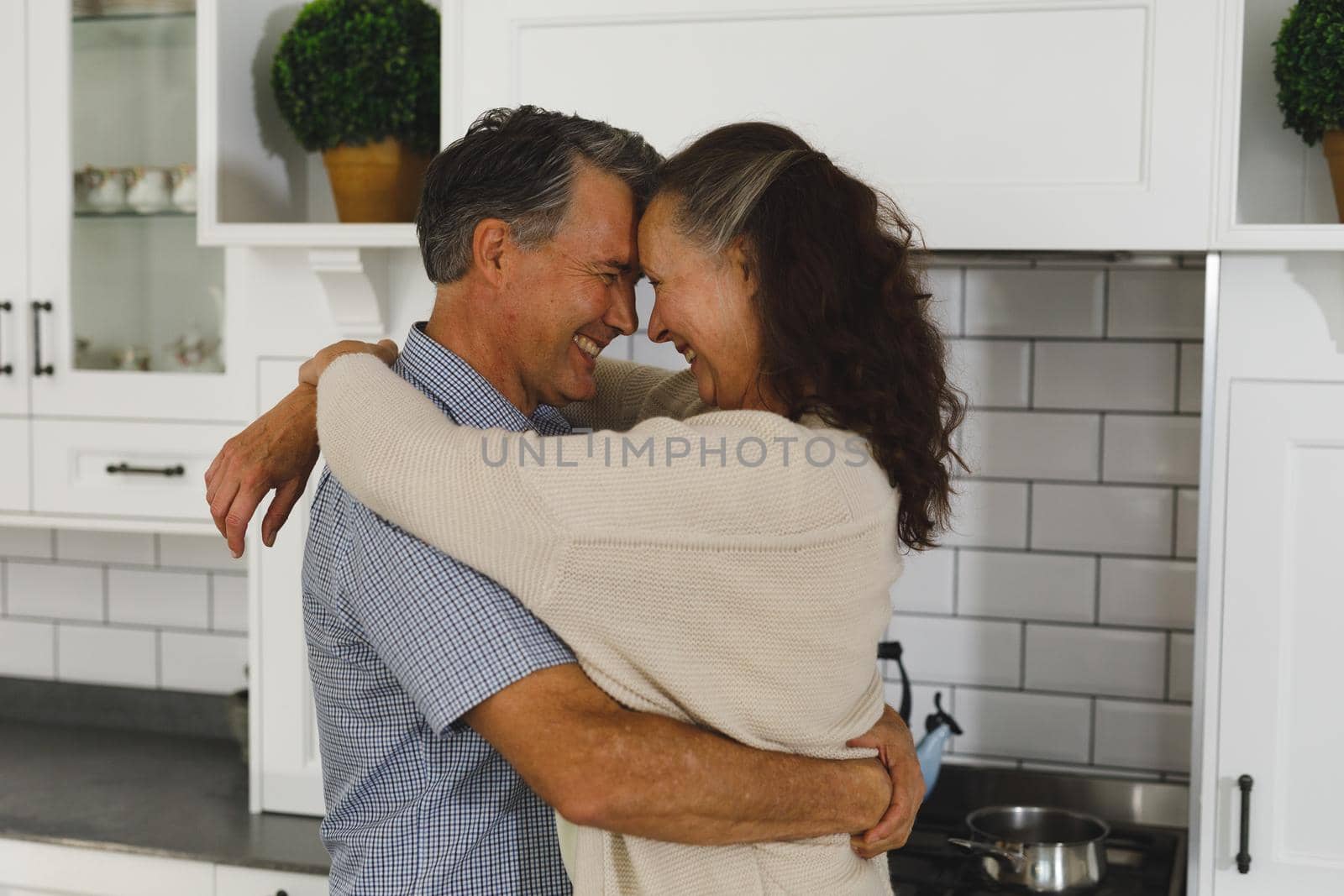 Happy senior caucasian couple in modern kitchen, embracing and smiling by Wavebreakmedia