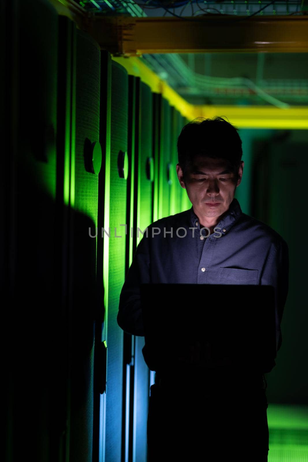 Asian male engineer using laptop in computer server room. database server management and maintenance concept