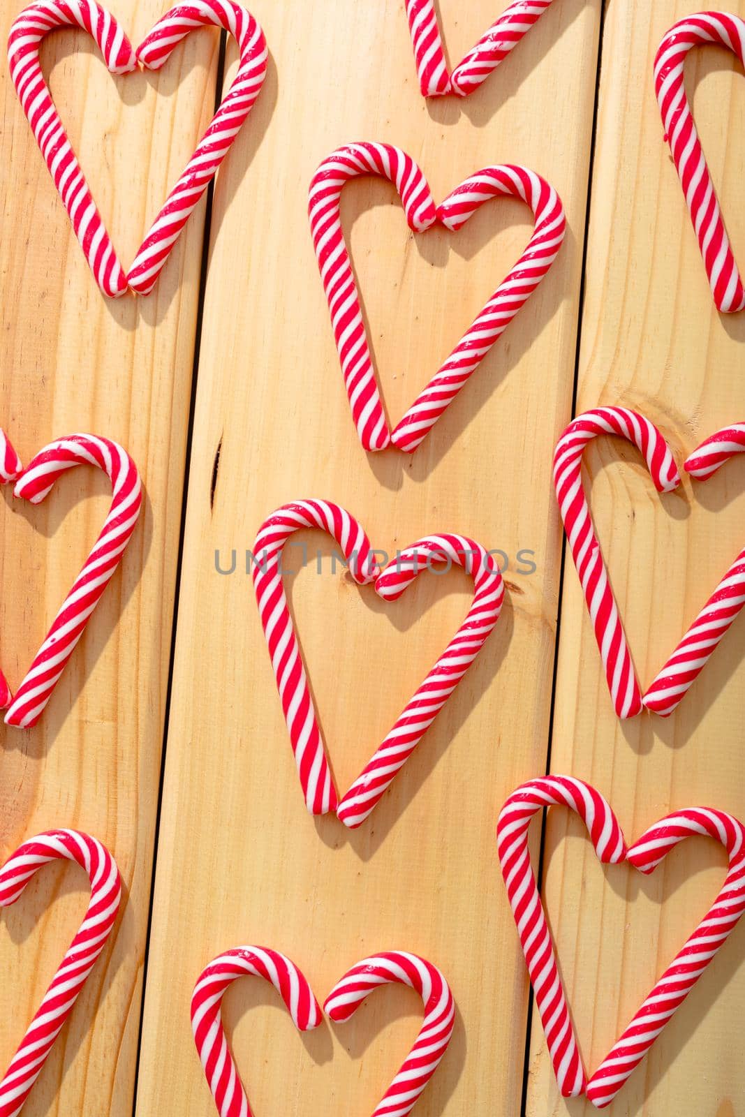 Composition of multiple candy canes in shape of heart on wooden background by Wavebreakmedia