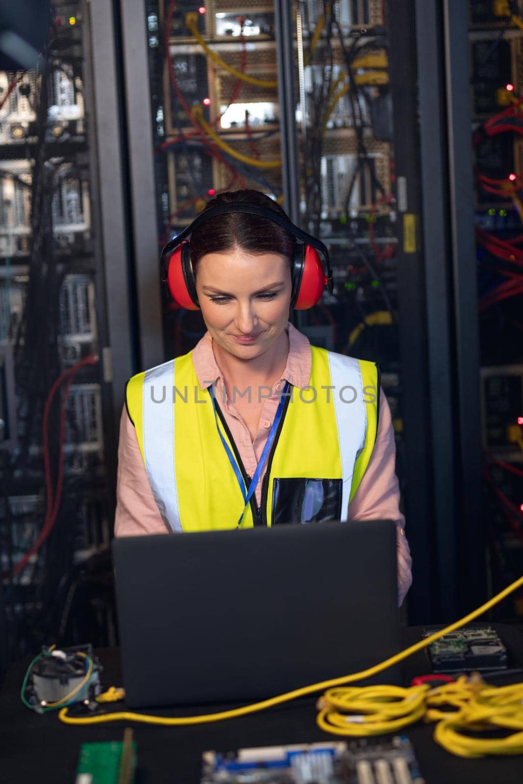 Caucasian female engineer wearing ear plugs using a laptop in computer server room by Wavebreakmedia