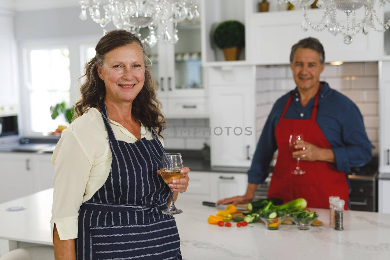 Portrait of happy senior caucasian couple in kitchen cooking together, drinking wine. retirement lifestyle, spending time at home.