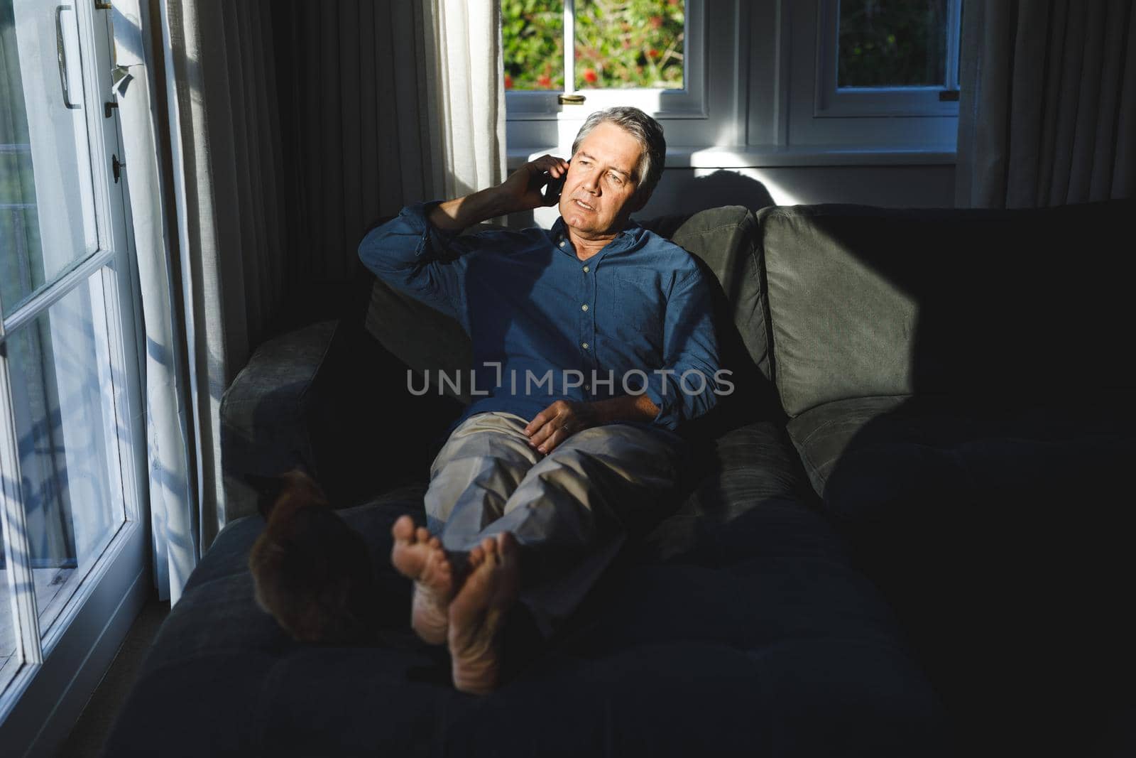 Senior caucasian man in living room sitting on sofa, talking on smartphone by Wavebreakmedia