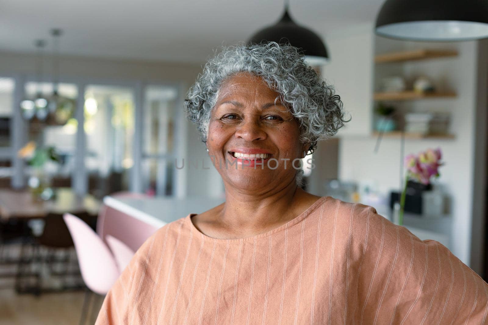 Happy african american senior woman standing standing in kitchen and looking at camera by Wavebreakmedia