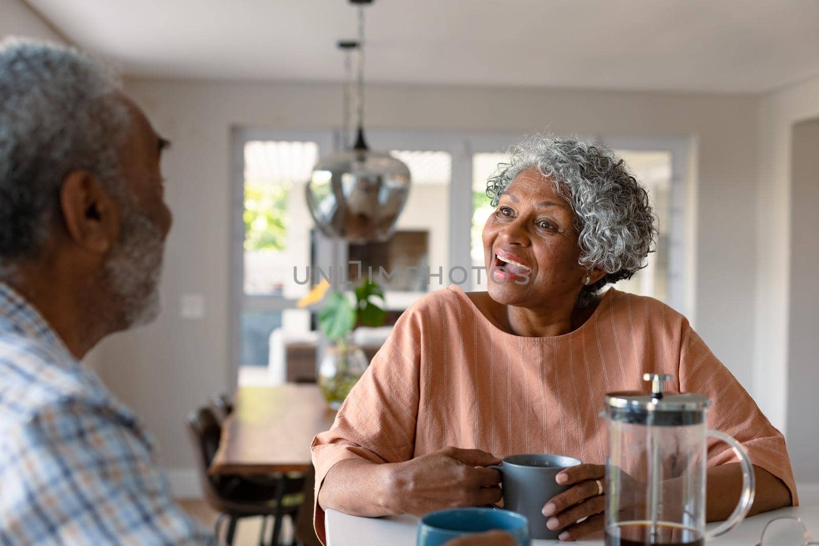 Happy african american senior couple sitting in kitchen with coffee and talking by Wavebreakmedia
