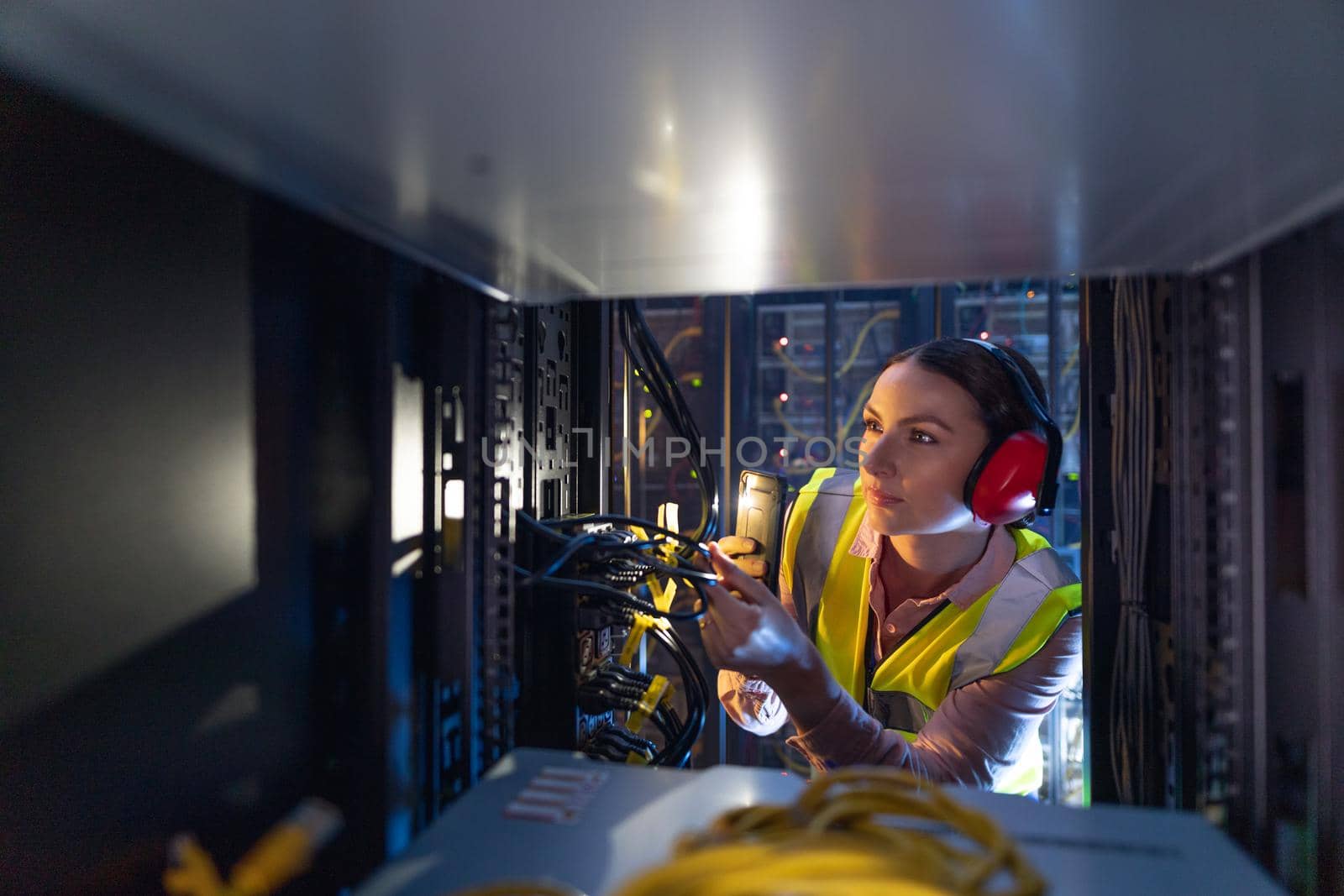 Caucasian female engineer using smartphone flash while inspecting the server in computer server room. database server management and maintenance concept