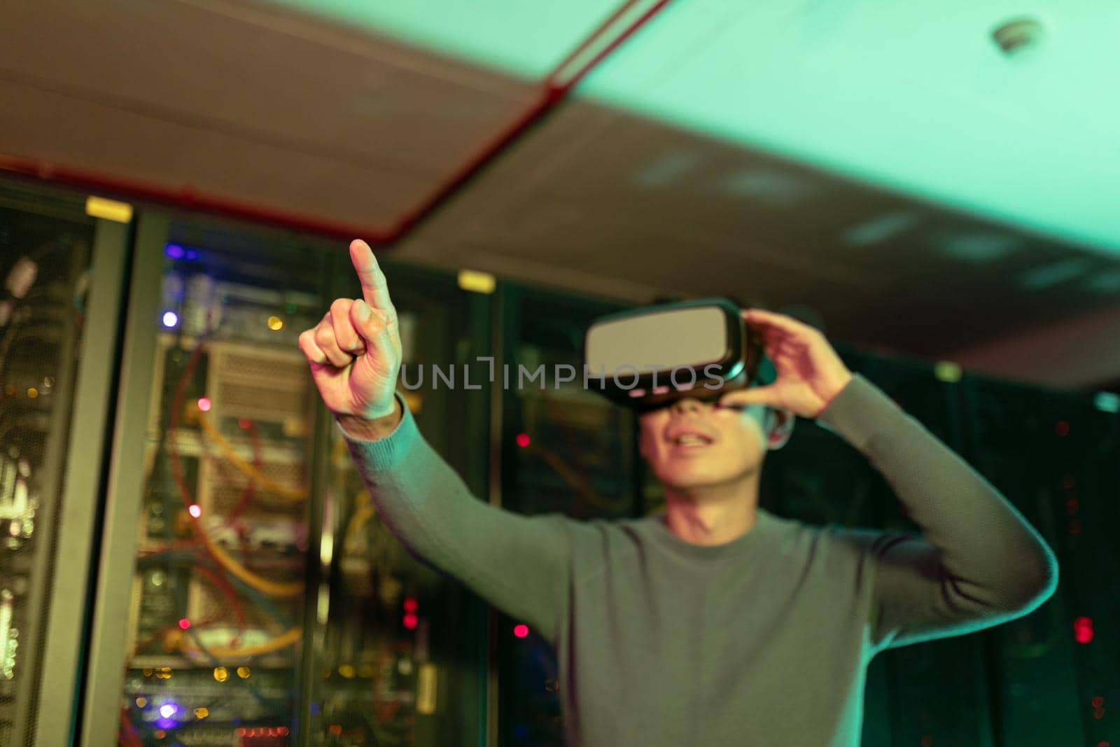Asian man wearing vr headset touching an invisible screen in computer server room. database server and futuristic technology concept