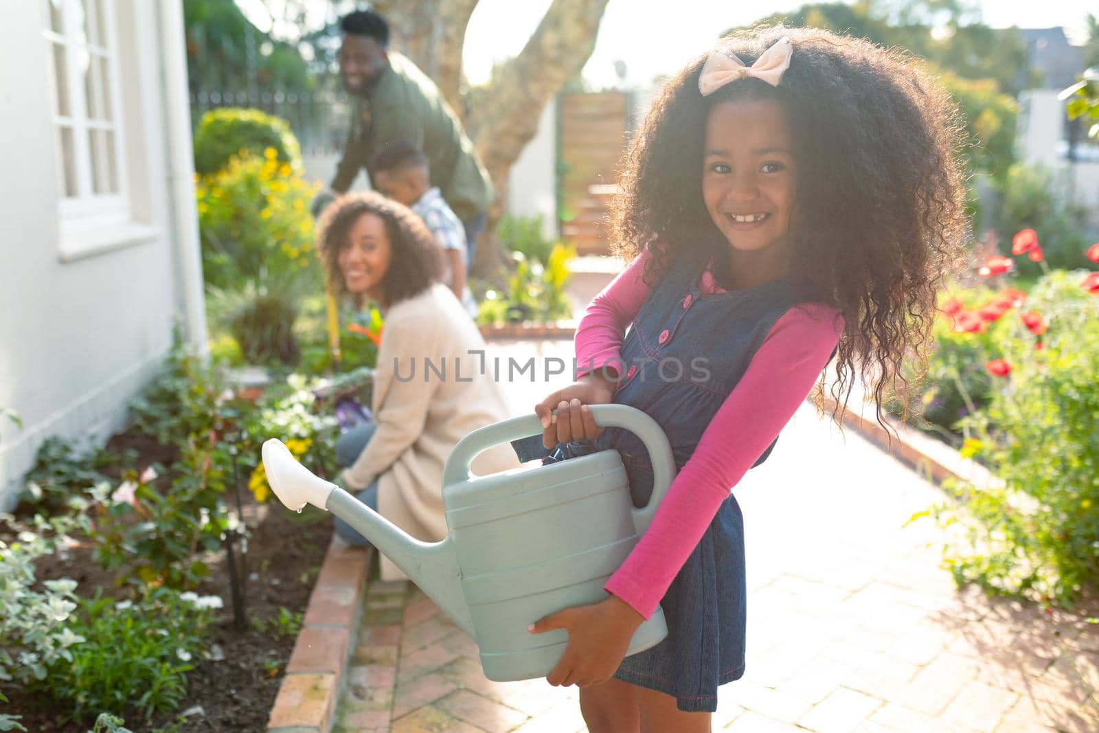 Happy african american girl and her family gardening and watering plants together by Wavebreakmedia