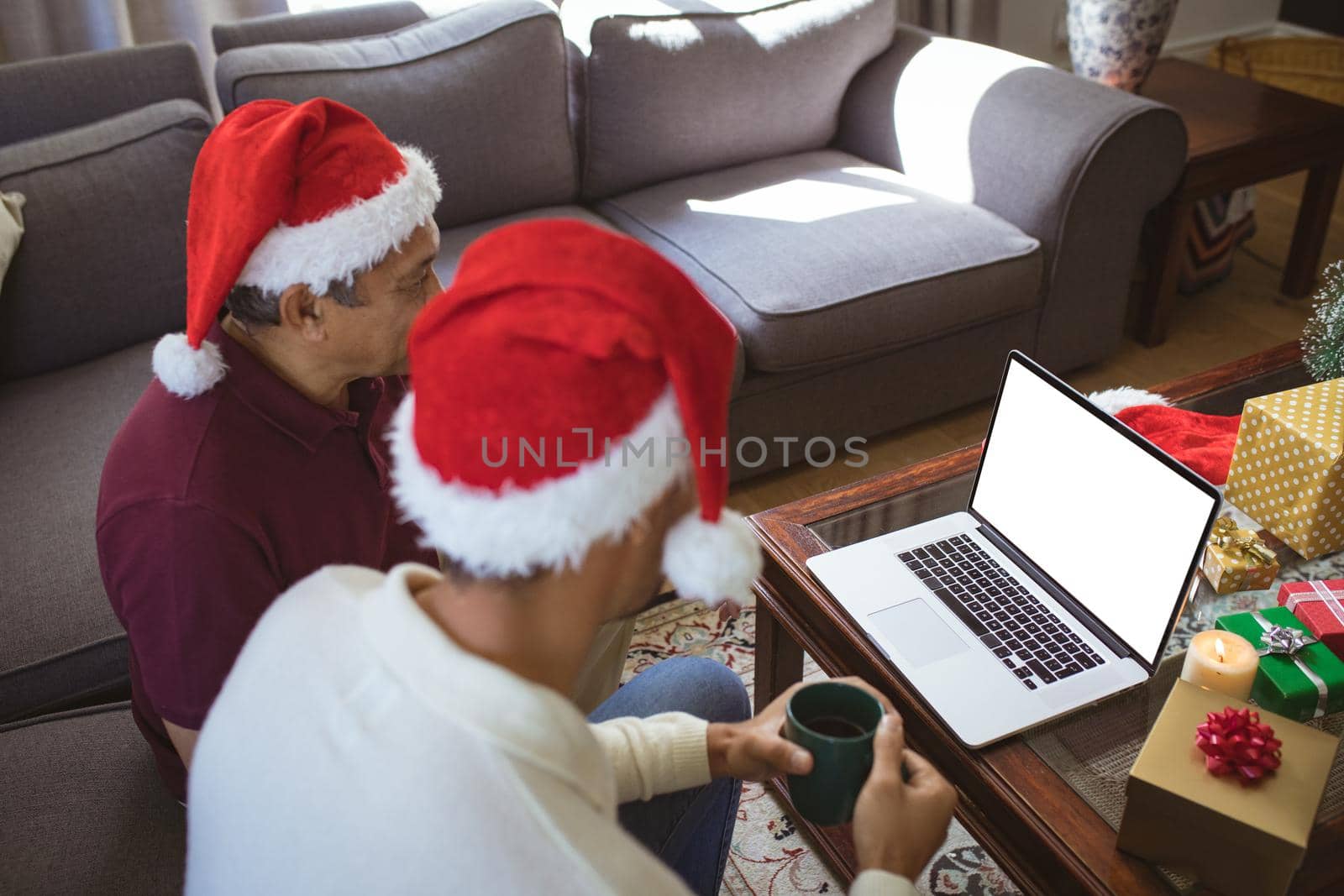Biracial adult son and senior father in santa hats making laptop christmas video call by Wavebreakmedia