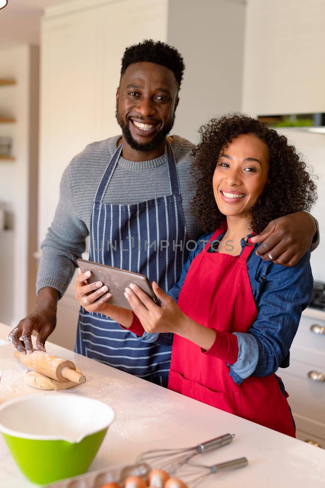 Happy african american couple wearing aprons, baking together and using tablet. family time, having fun together at home.