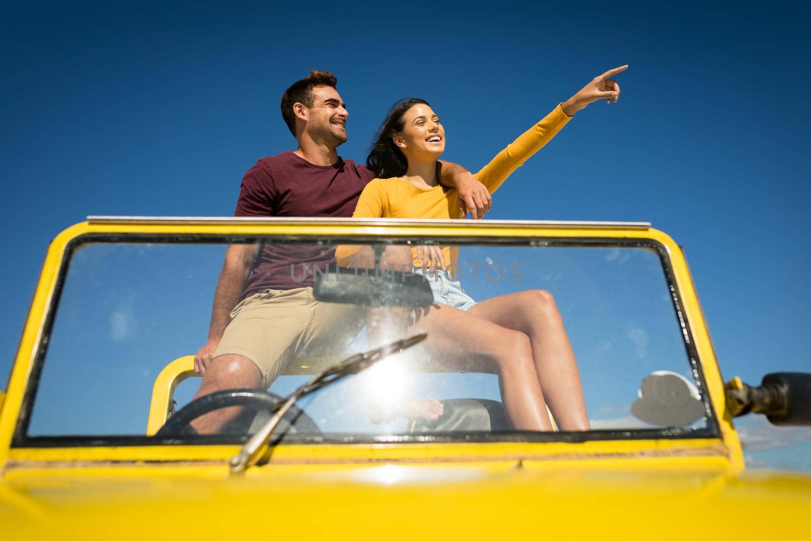 Happy caucasian couple sitting in beach buggy by the sea pointing. beach break on summer holiday road trip.