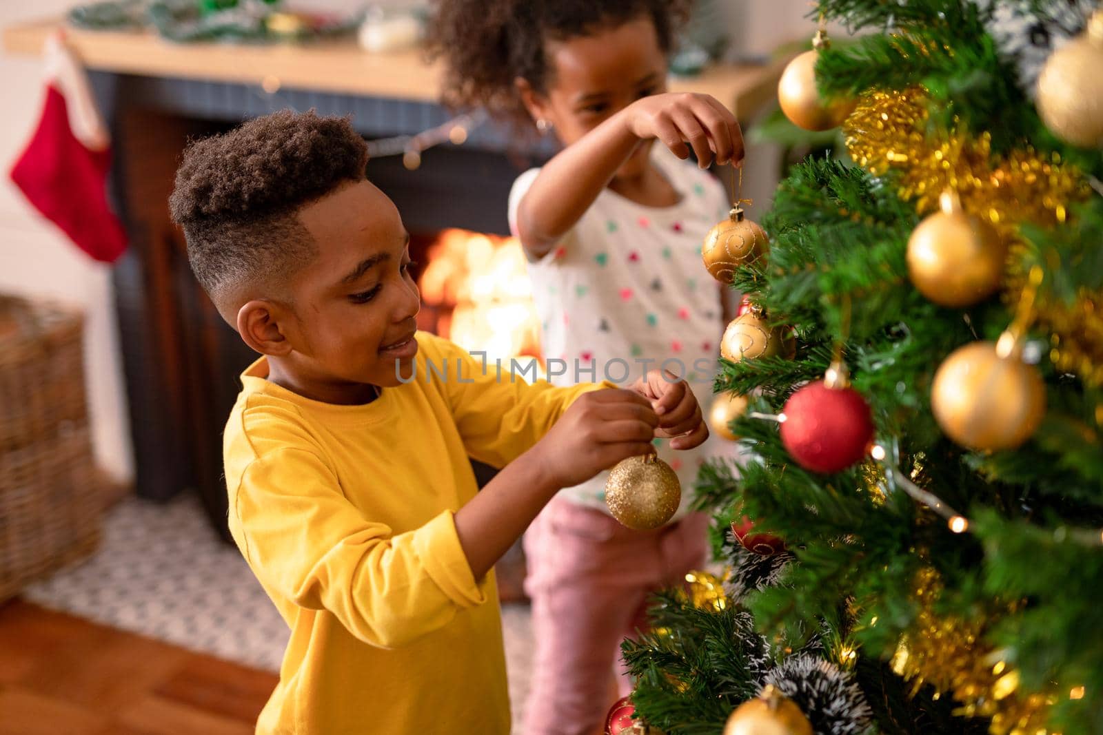 Happy african american siblings hanging baubles, decorating christmas tree by Wavebreakmedia