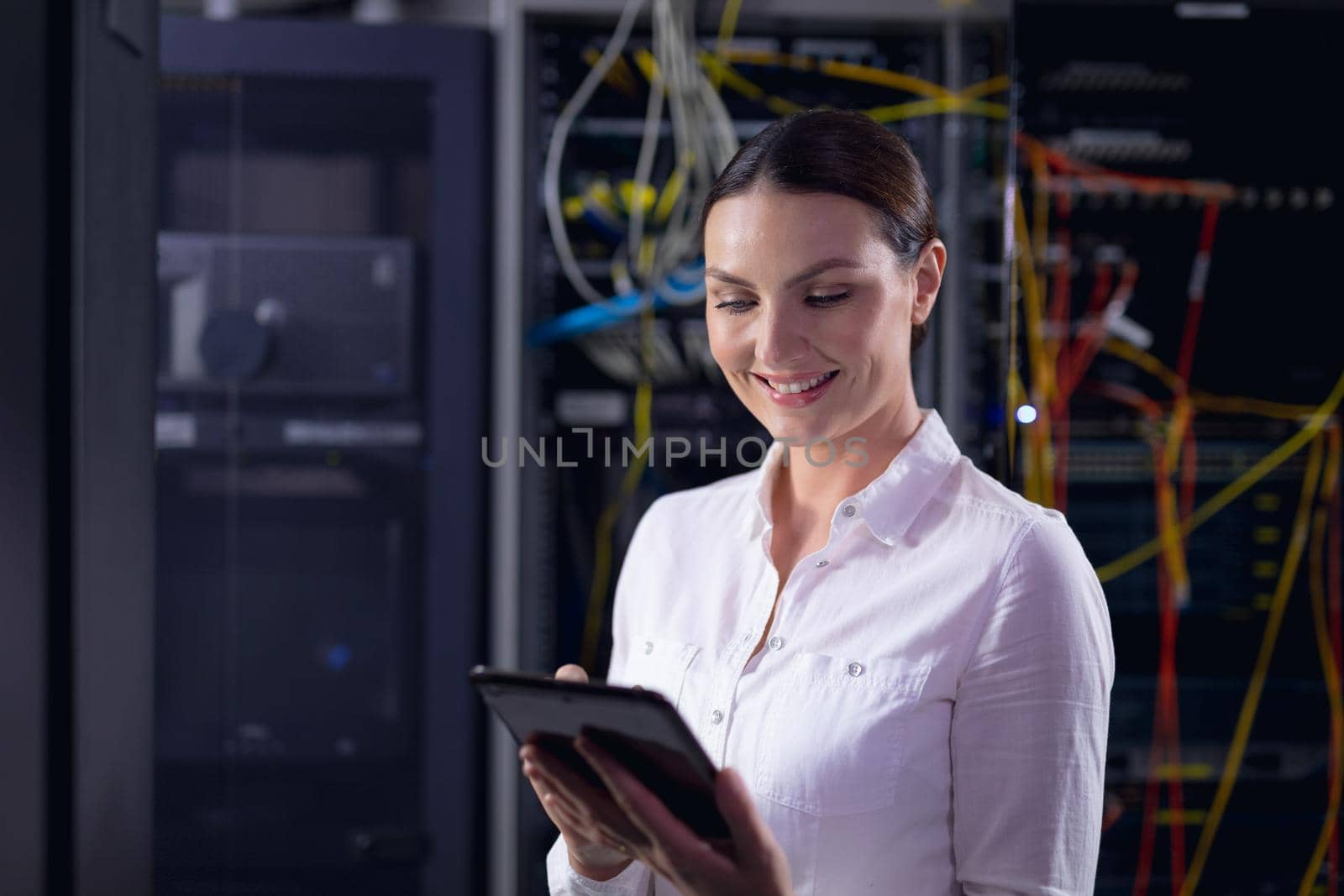 Caucasian female engineer smiling while using digital tablet in computer server room. database server management and maintenance concept