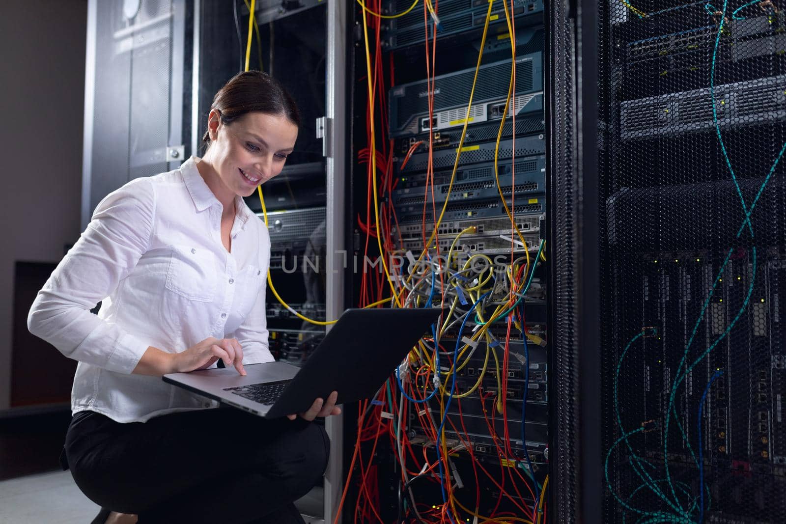 Caucasian female engineer using laptop and inspecting computer server in computer server room. database server management and maintenance concept