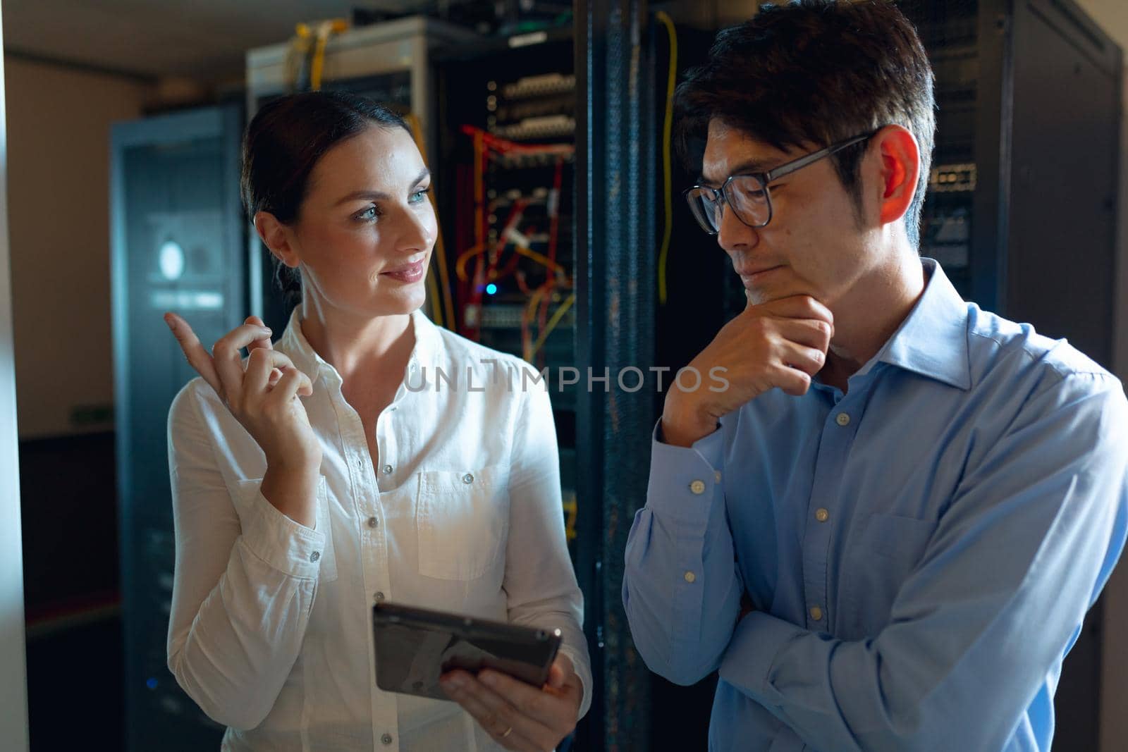 Diverse male and female engineers with digital tablet discussing in computer server room. database server management and maintenance concept