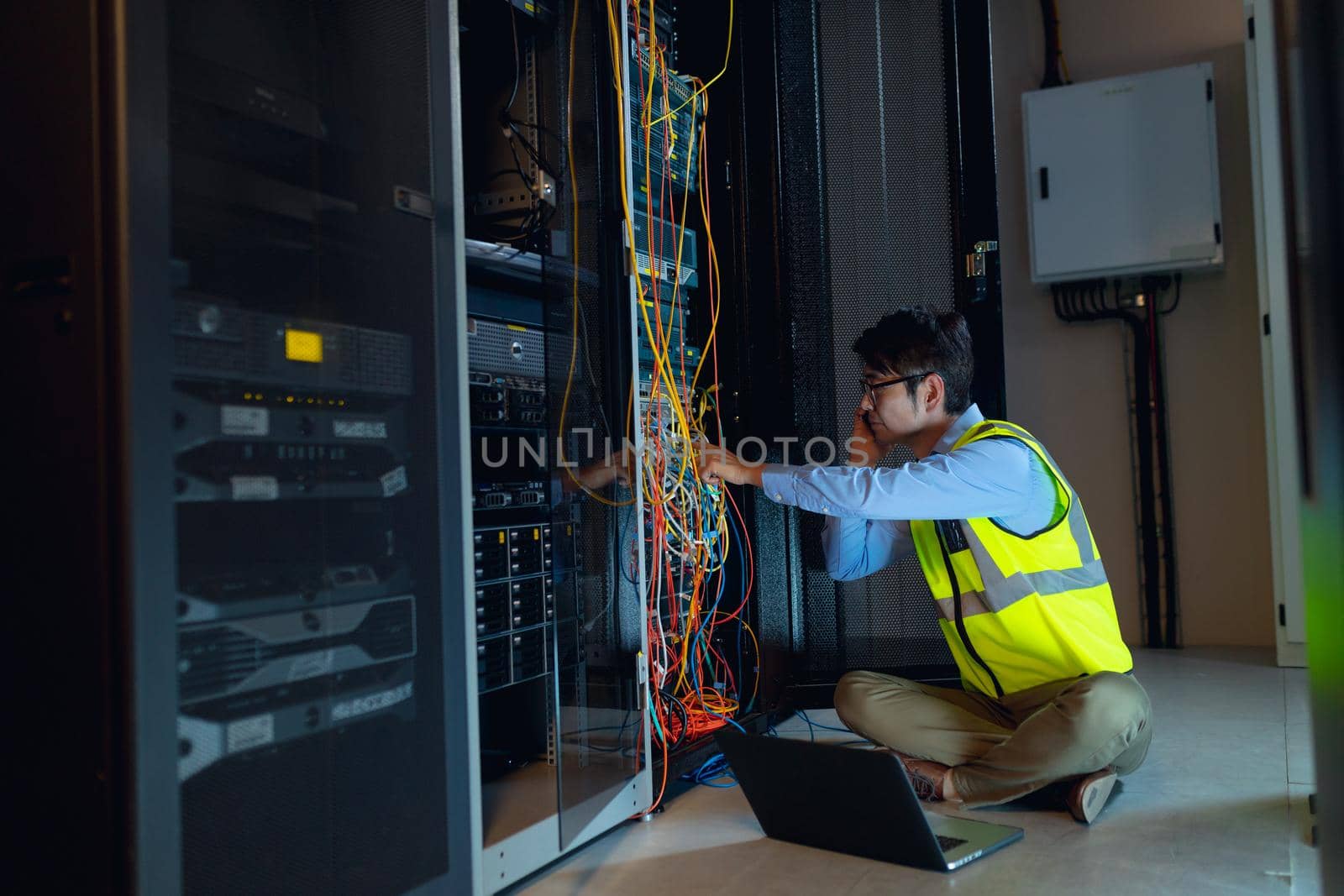Asian male engineer with laptop talking on smartphone while inspecting in computer server room by Wavebreakmedia