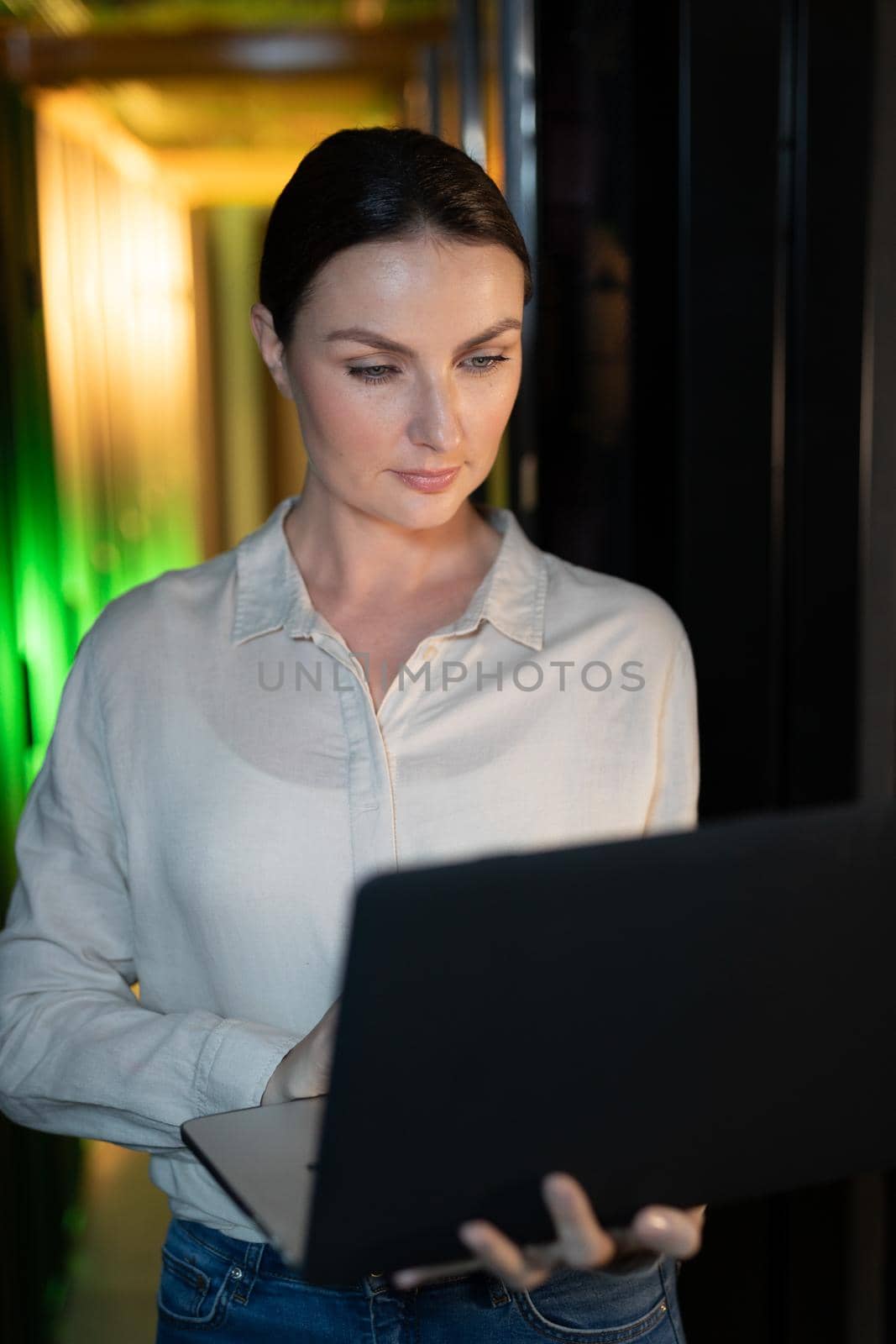 Caucasian female engineer using laptop in computer server room. database server management and maintenance concept