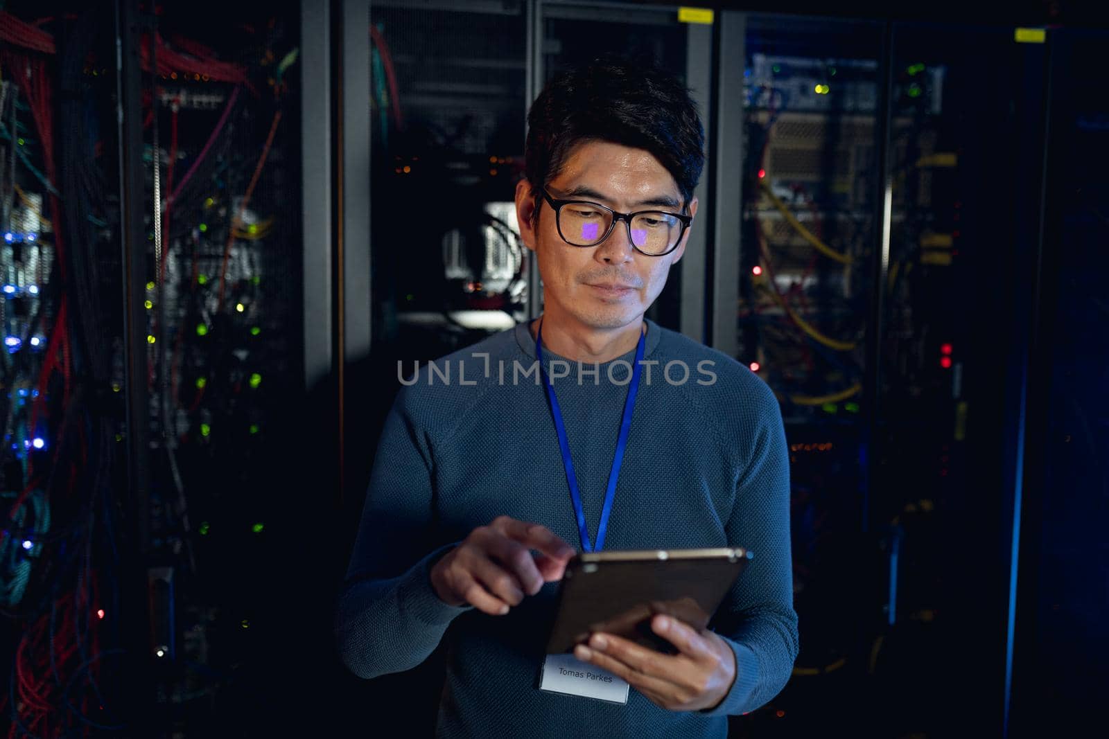 Asian male engineer using digital tablet in computer server room. database server management and maintenance concept