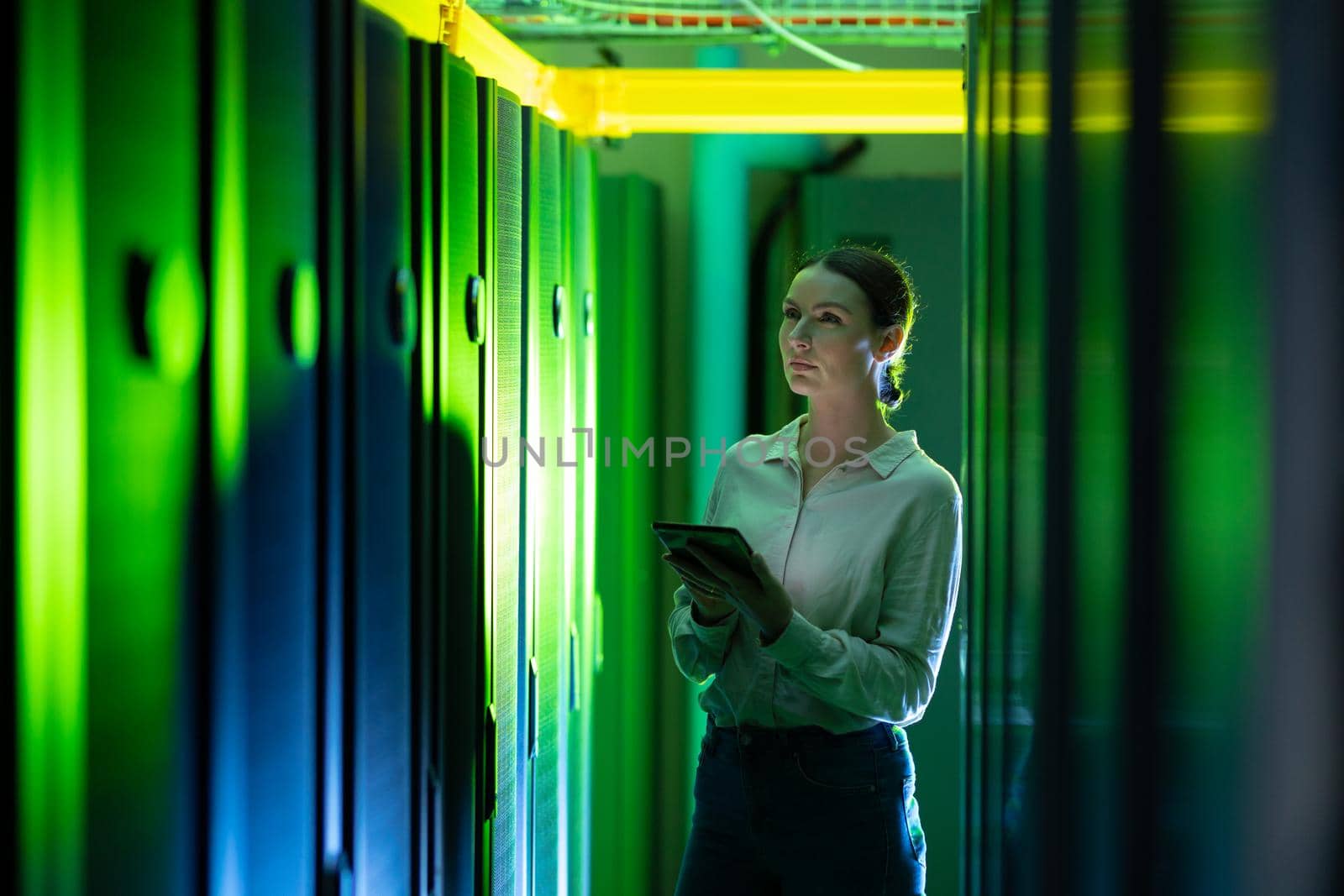 Caucasian female engineer using digital tablet while inspecting in computer server room. database server management and maintenance concept