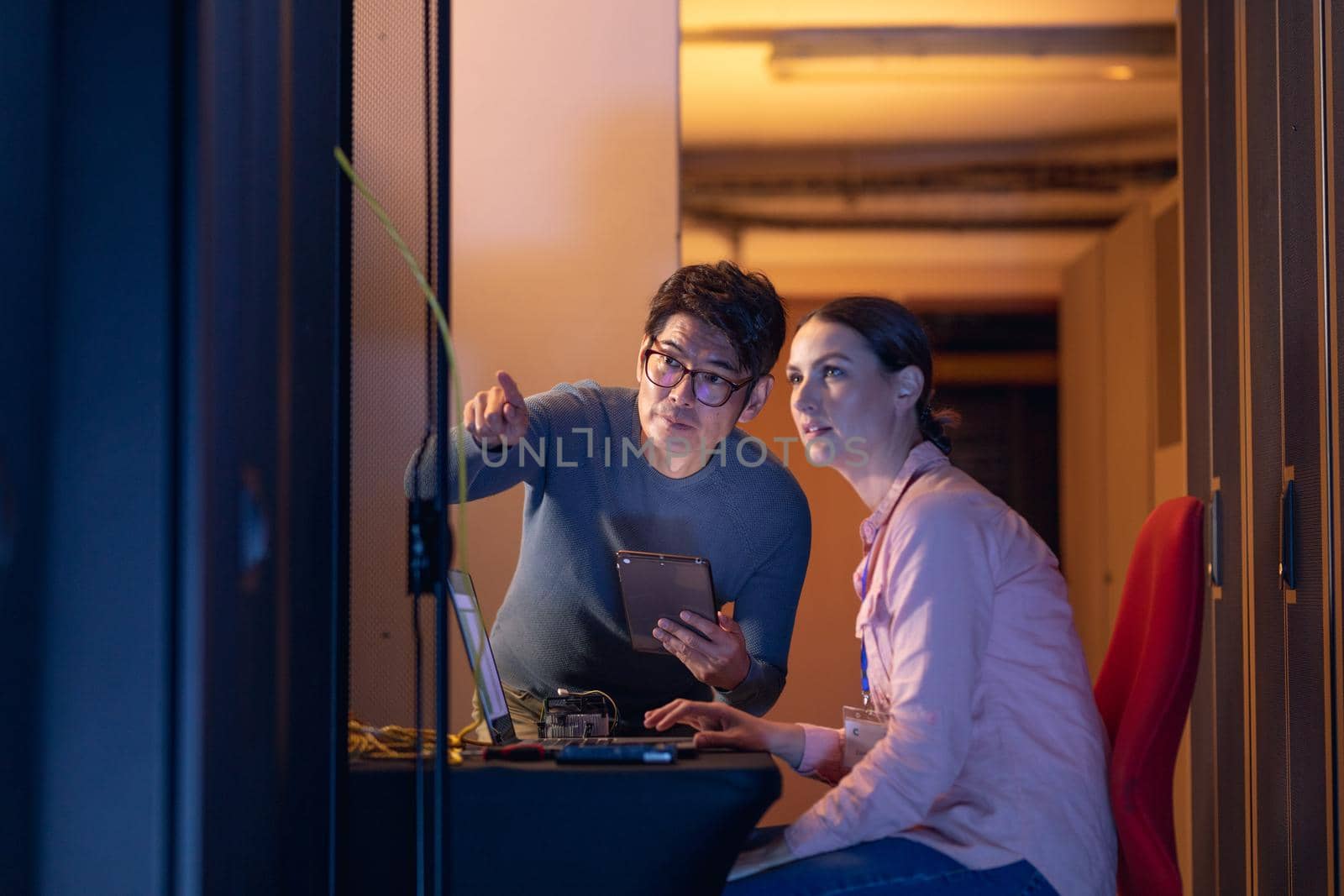 Diverse male and female engineers discussing over a digital tablet while inspecting in server room. database server management and maintenance concept