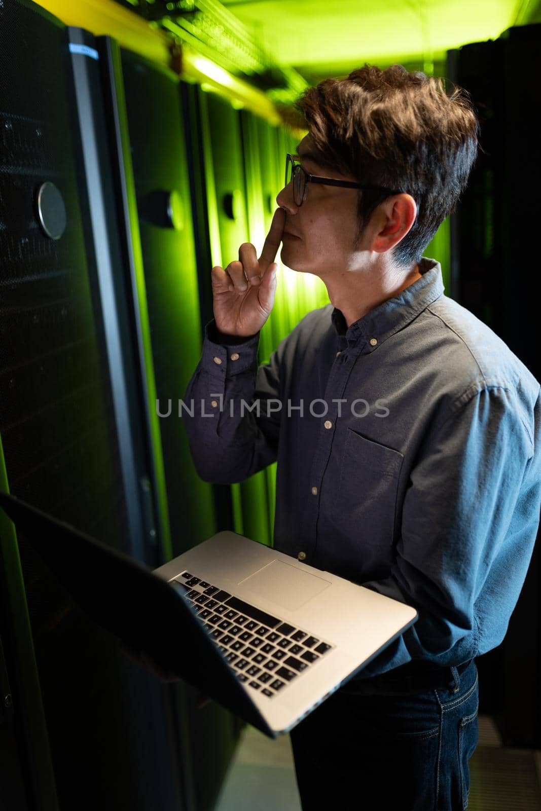Thoughtful asian male engineer with laptop inspecting in computer server room by Wavebreakmedia
