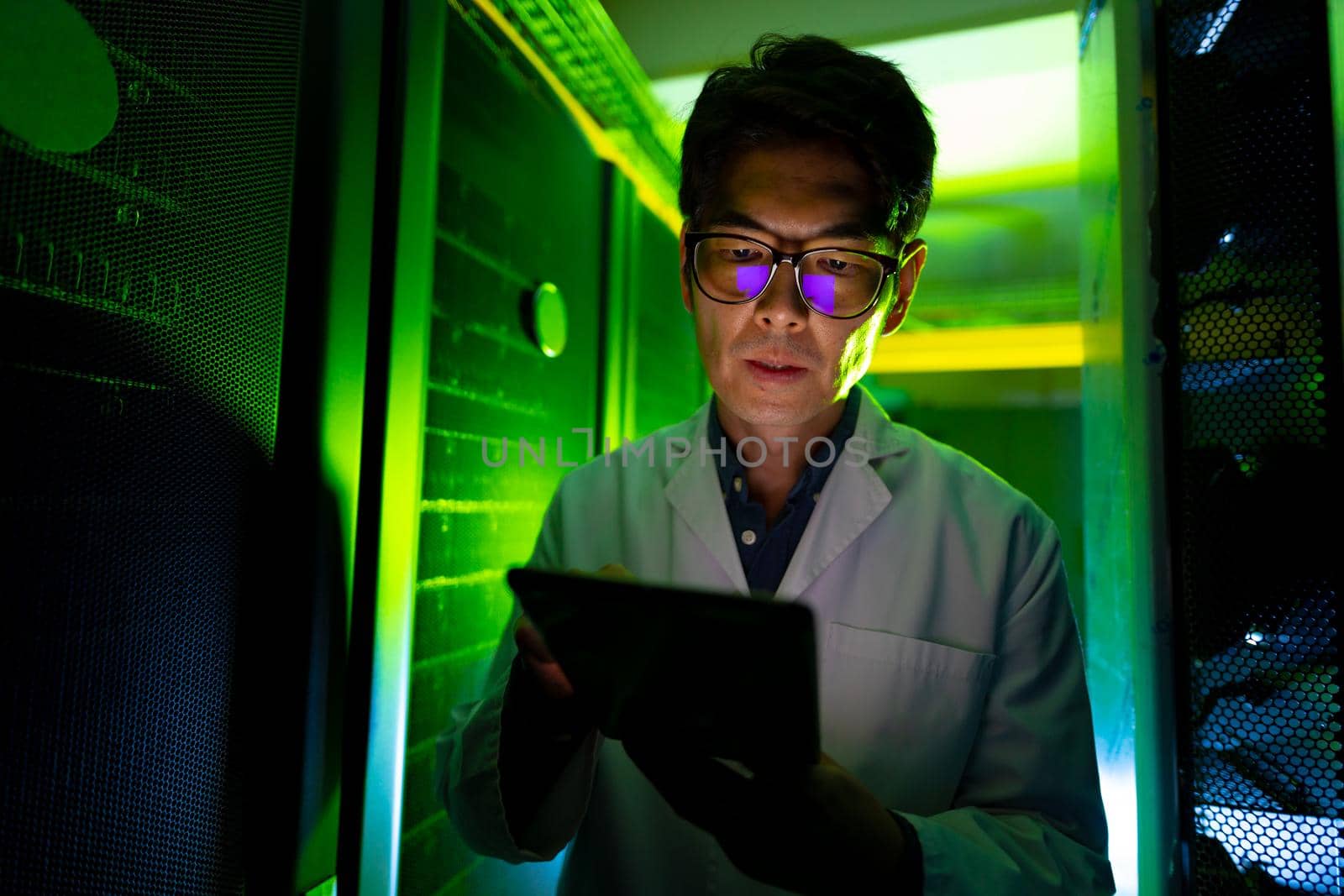 Asian male engineer wearing an apron using digital tablet in computer server room. database server management and maintenance concept