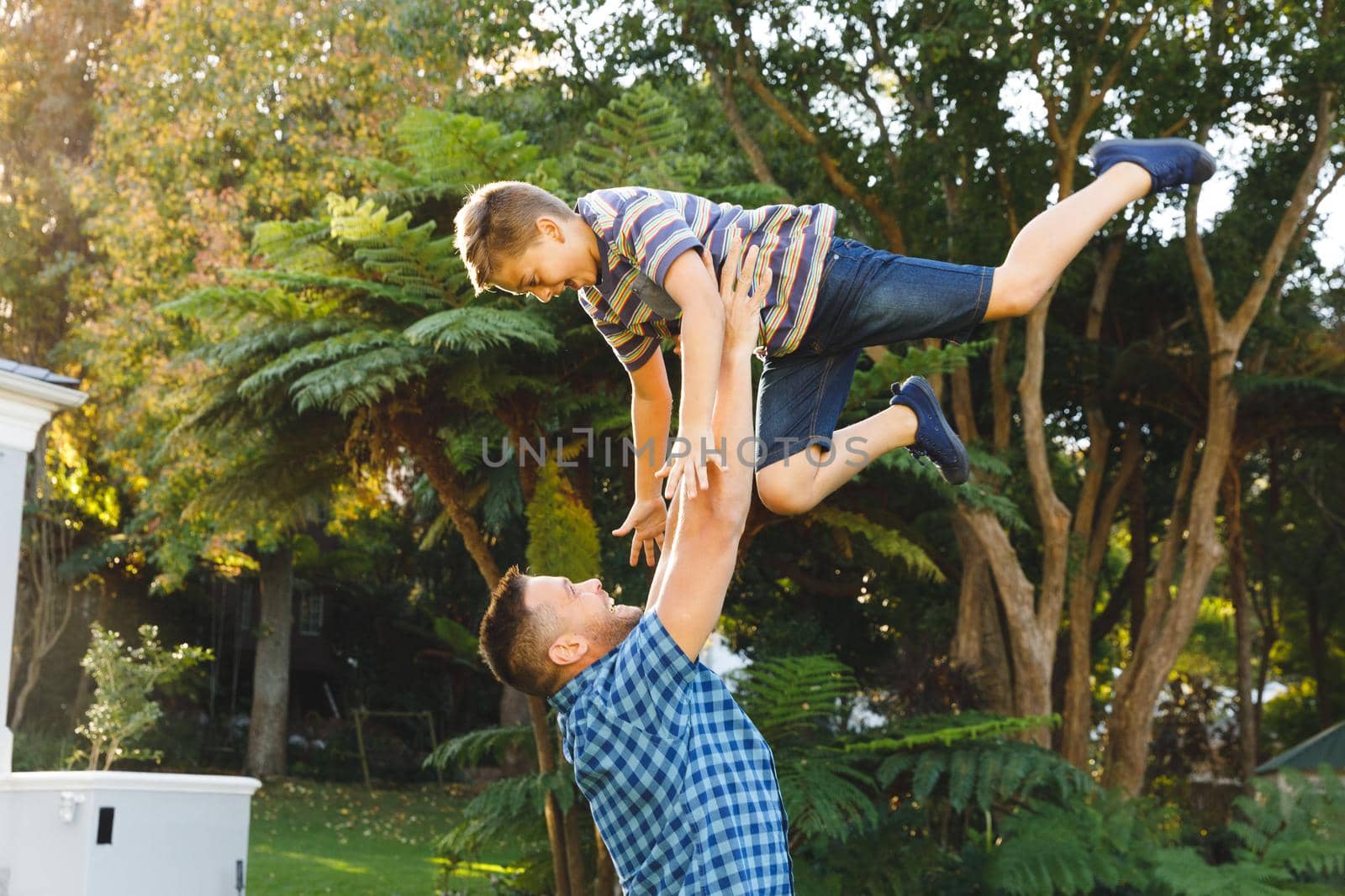 Smiling caucasian father lifting his son up outside house in sunny garden by Wavebreakmedia