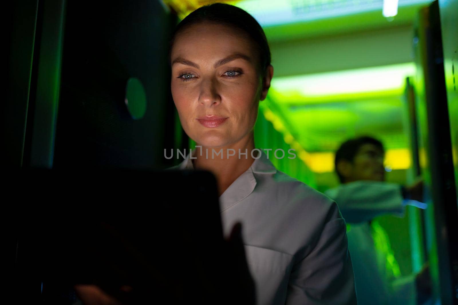 Caucasian female engineer wearing an apron using laptop in computer server room. database server management and maintenance concept