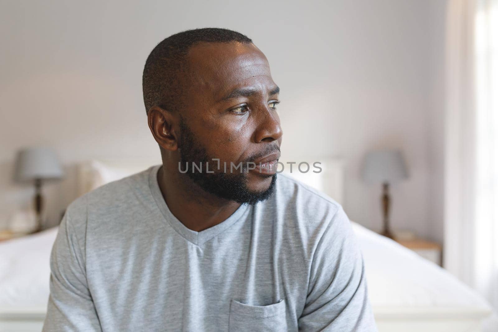 Thoughtful african american man sitting on bed and looking away in bedroom by Wavebreakmedia