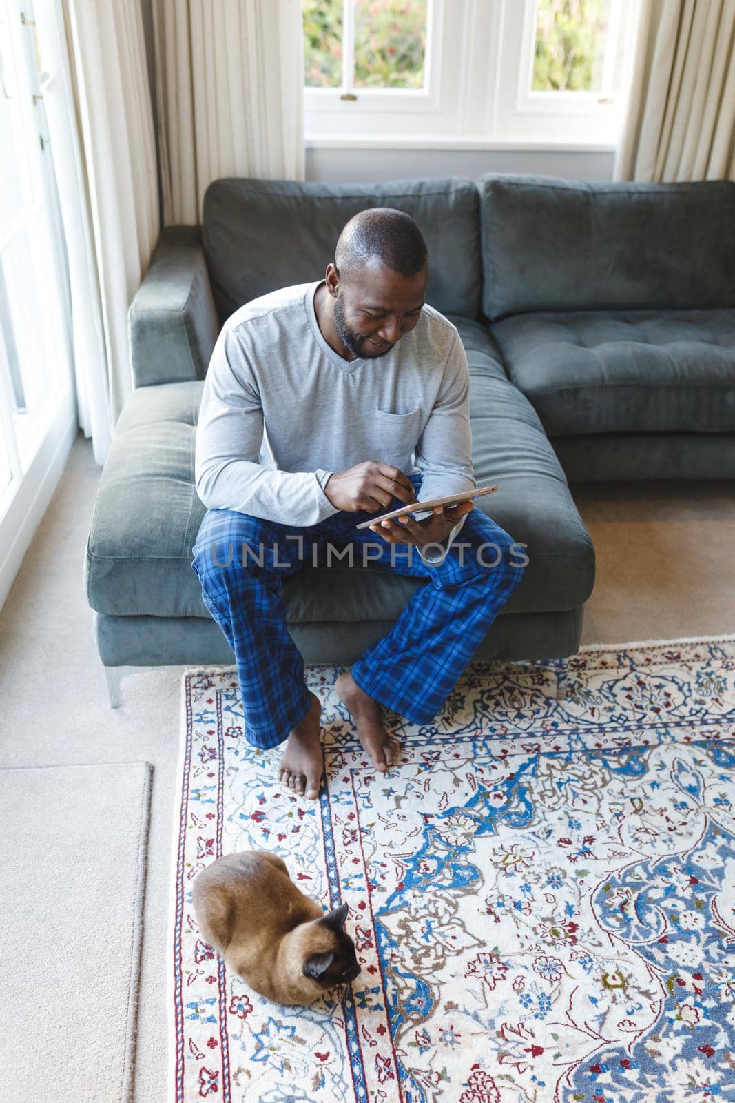 African american man using tablet and sitting on couch in living room. spending time alone at home with technology.