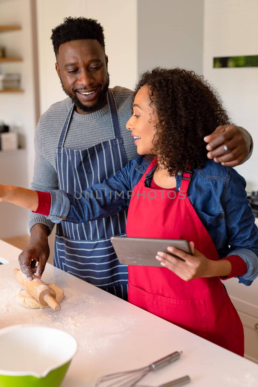 Happy african american couple wearing aprons, baking together and using tablet. family time, having fun together at home.