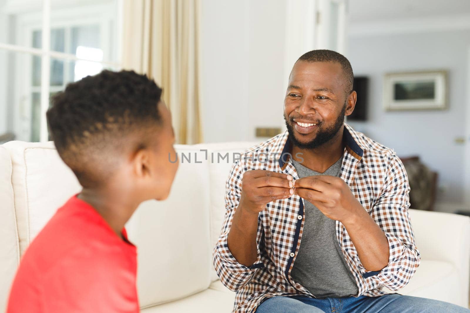 Happy african american father with son sitting on couch in living room talking sign language by Wavebreakmedia