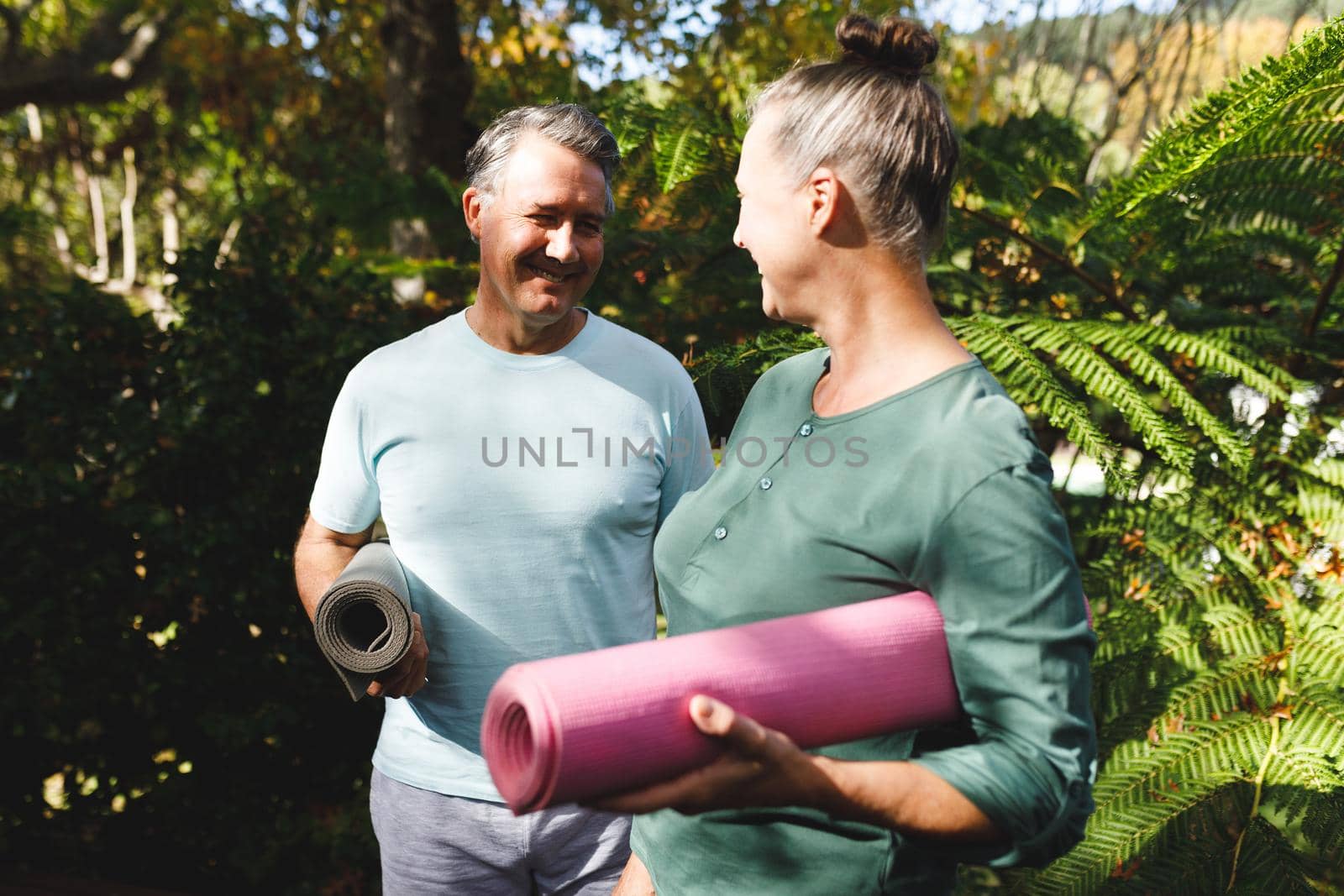 Happy senior caucasian couple practicing yoga, holding yoga mats in sunny garden by Wavebreakmedia