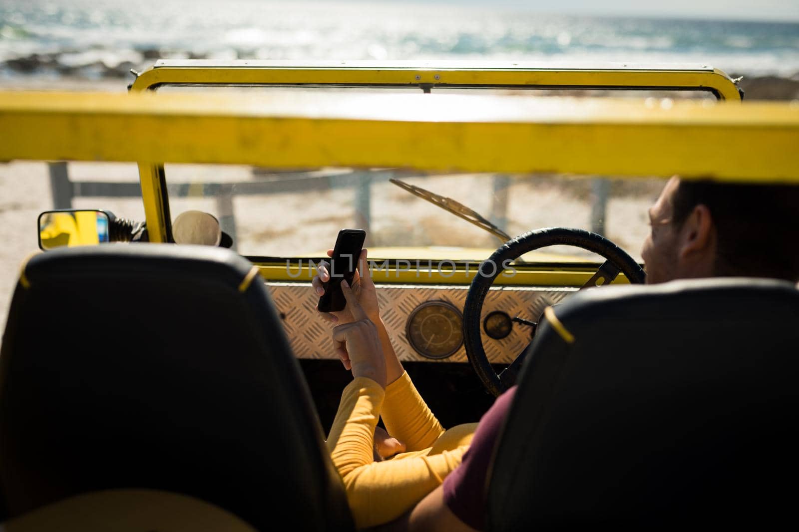 Caucasian couple lying on a beach buggy by the sea using smartphone. beach break on summer holiday road trip.