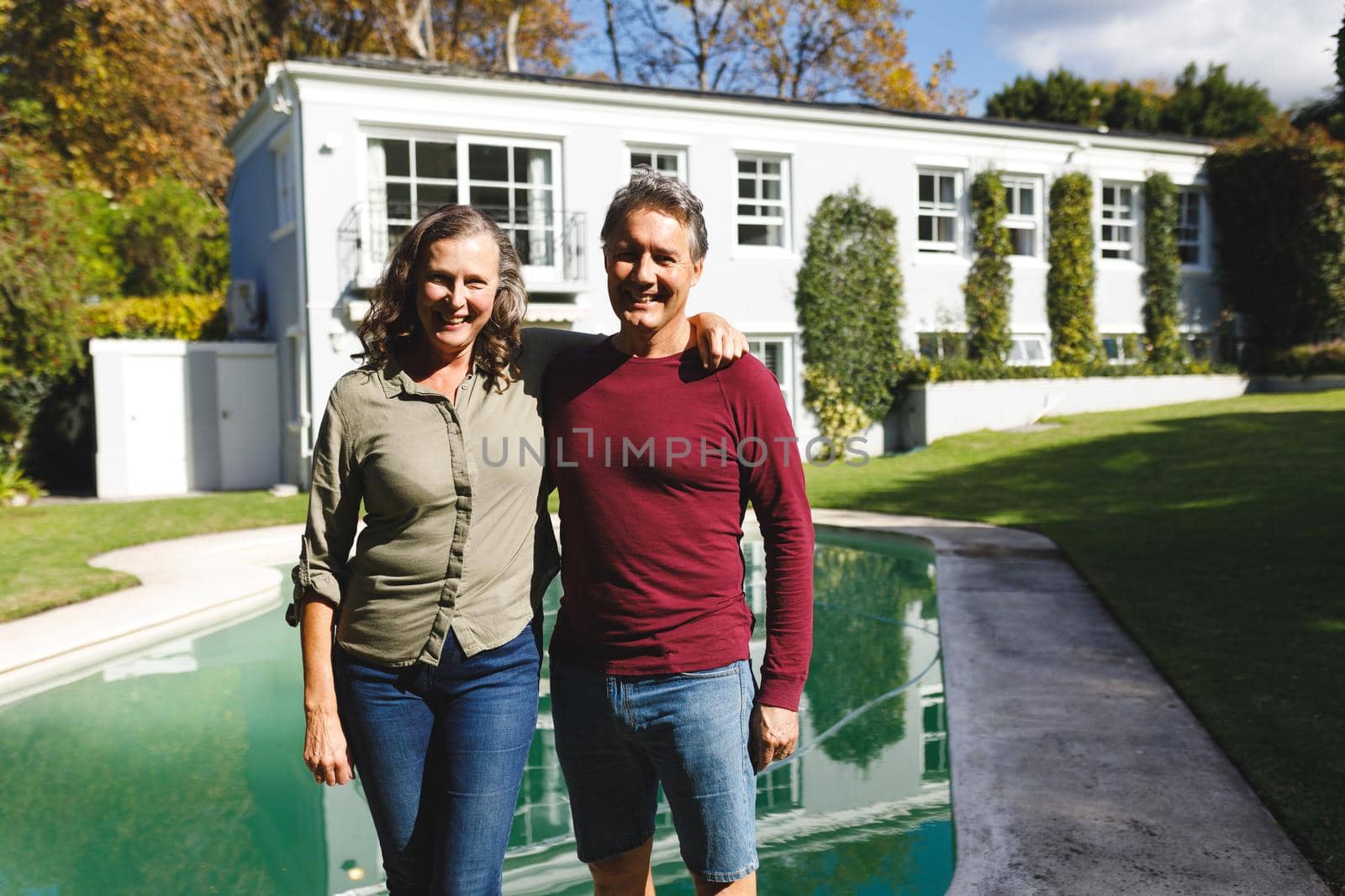 Portrait of happy senior caucasian couple embracing, looking to camera in sunny garden. luxury retirement lifestyle, spending time at home.