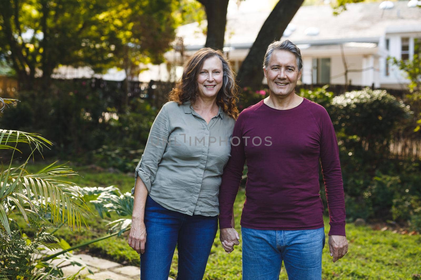 Portrait of happy senior caucasian couple holding hands, looking to camera in garden. retirement lifestyle, spending time at home.
