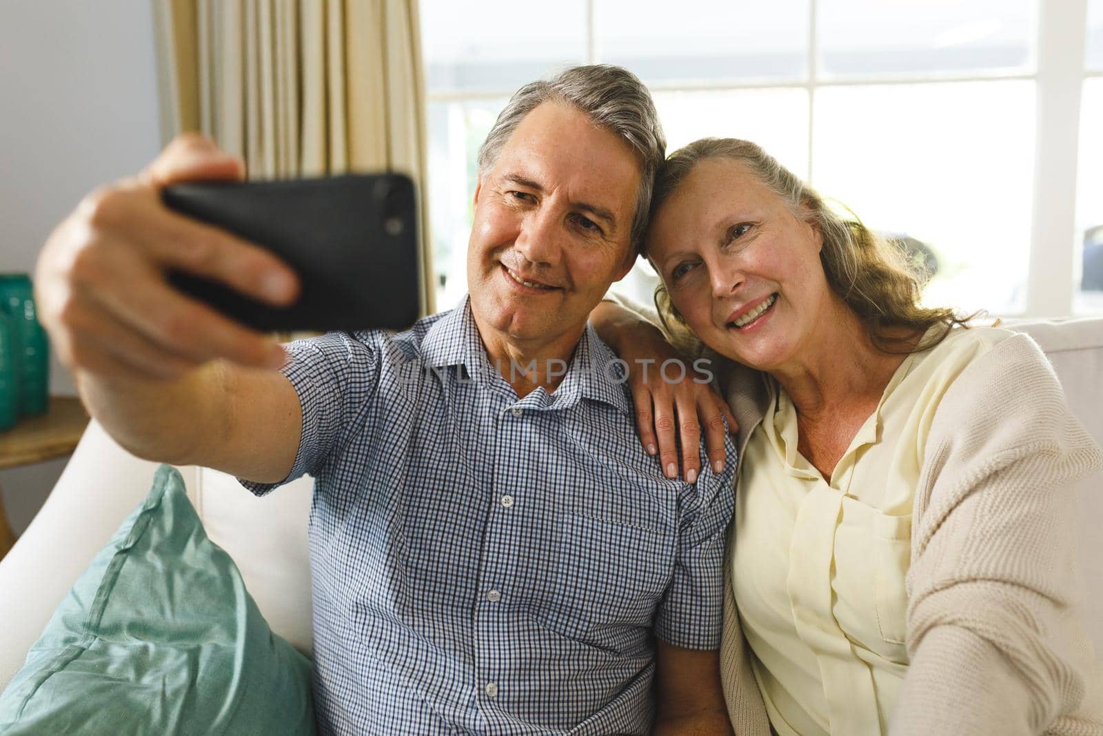 Happy senior caucasian couple in living room, sitting on sofa, taking selfies and smiling by Wavebreakmedia