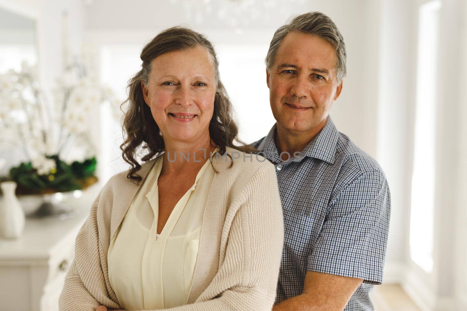 Portrait of happy senior caucasian couple in living room, embracing and smiling. retirement lifestyle, spending time at home.