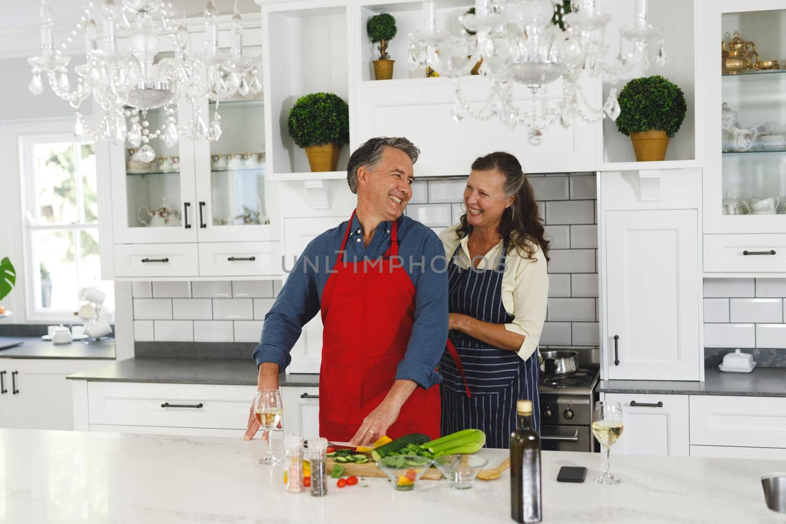 Happy senior caucasian couple wearing aprons in modern kitchen. retirement lifestyle, spending time at home.