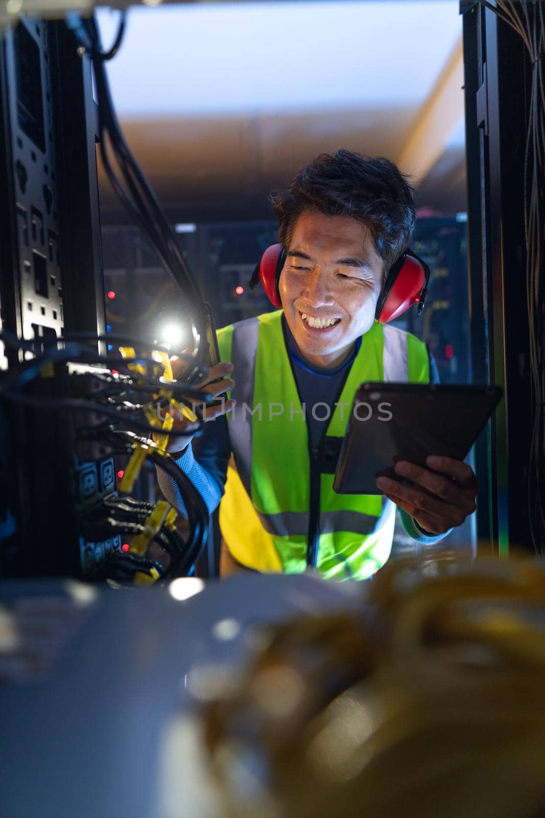 Asian male engineer using smartphone flash while inspecting the server in computer server room. database server management and maintenance concept