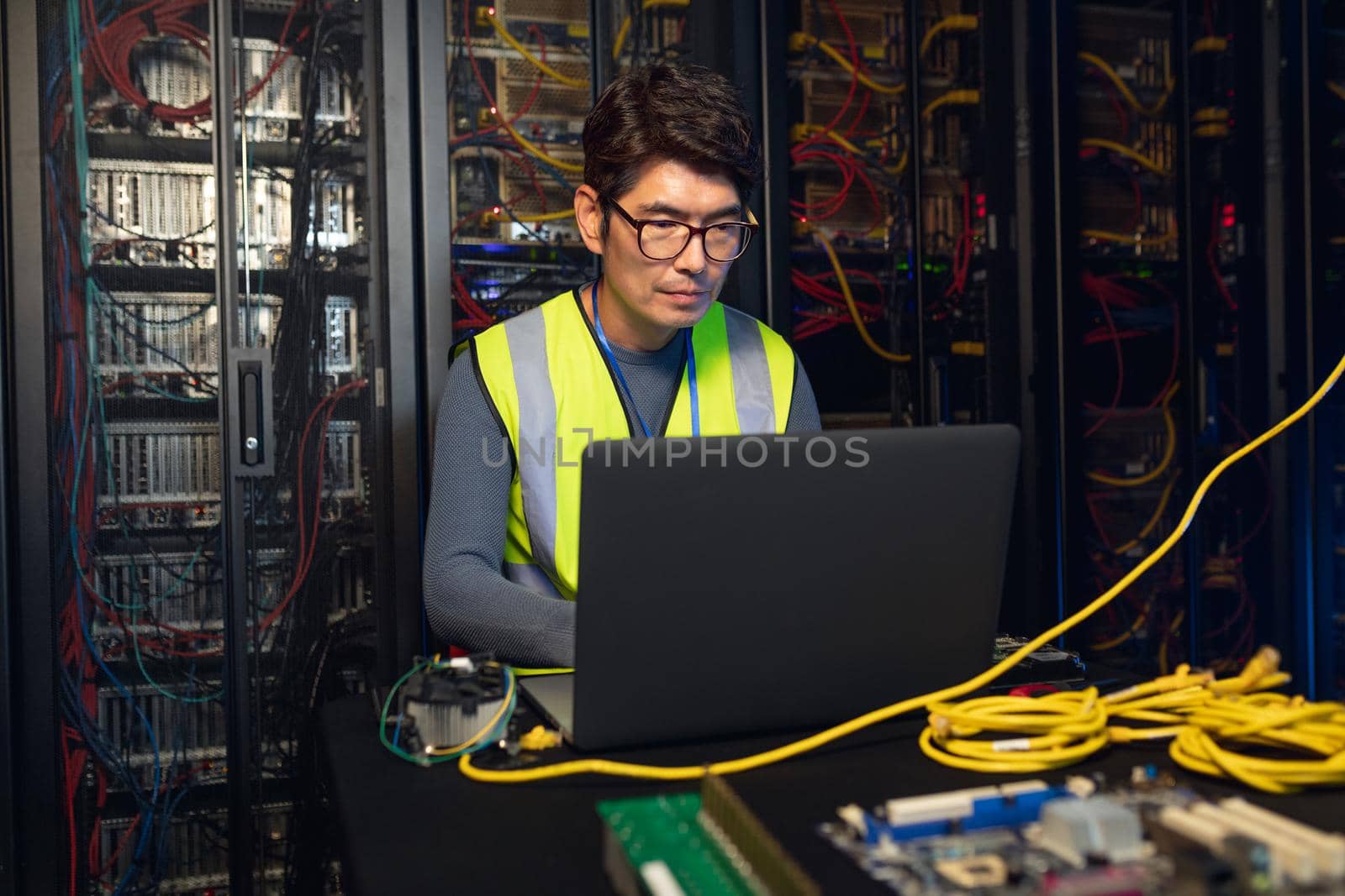 Asian male engineer using a laptop in computer server room by Wavebreakmedia