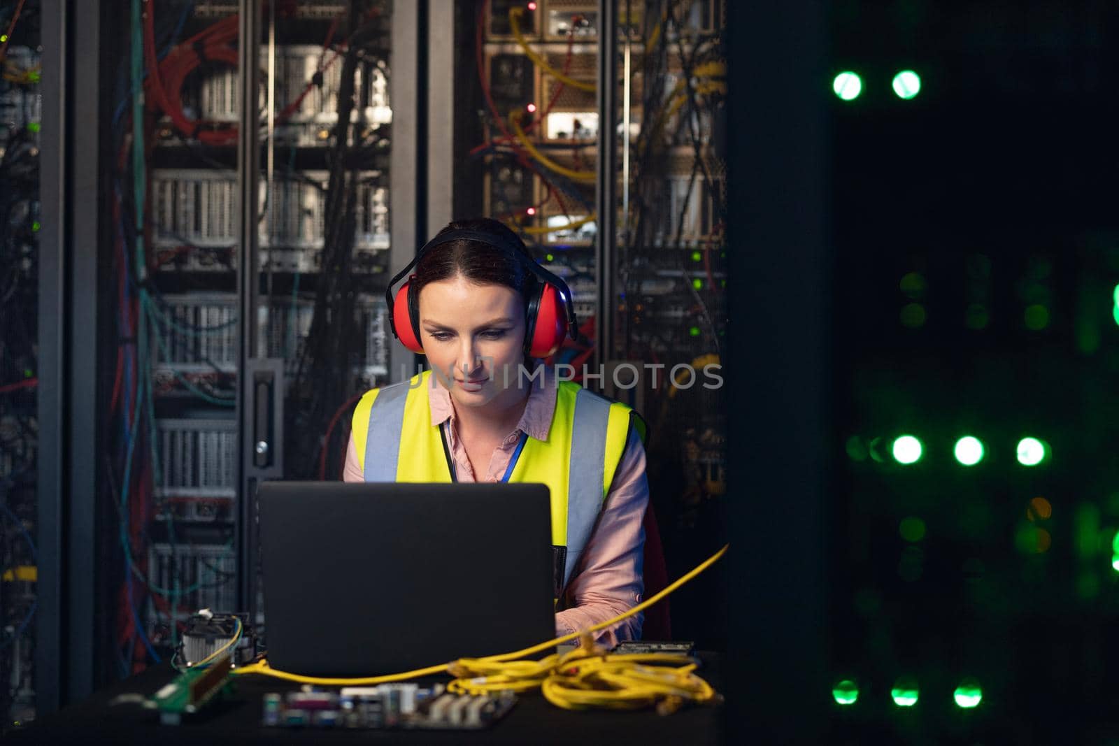 Caucasian female engineer wearing ear plugs using a laptop in computer server room by Wavebreakmedia