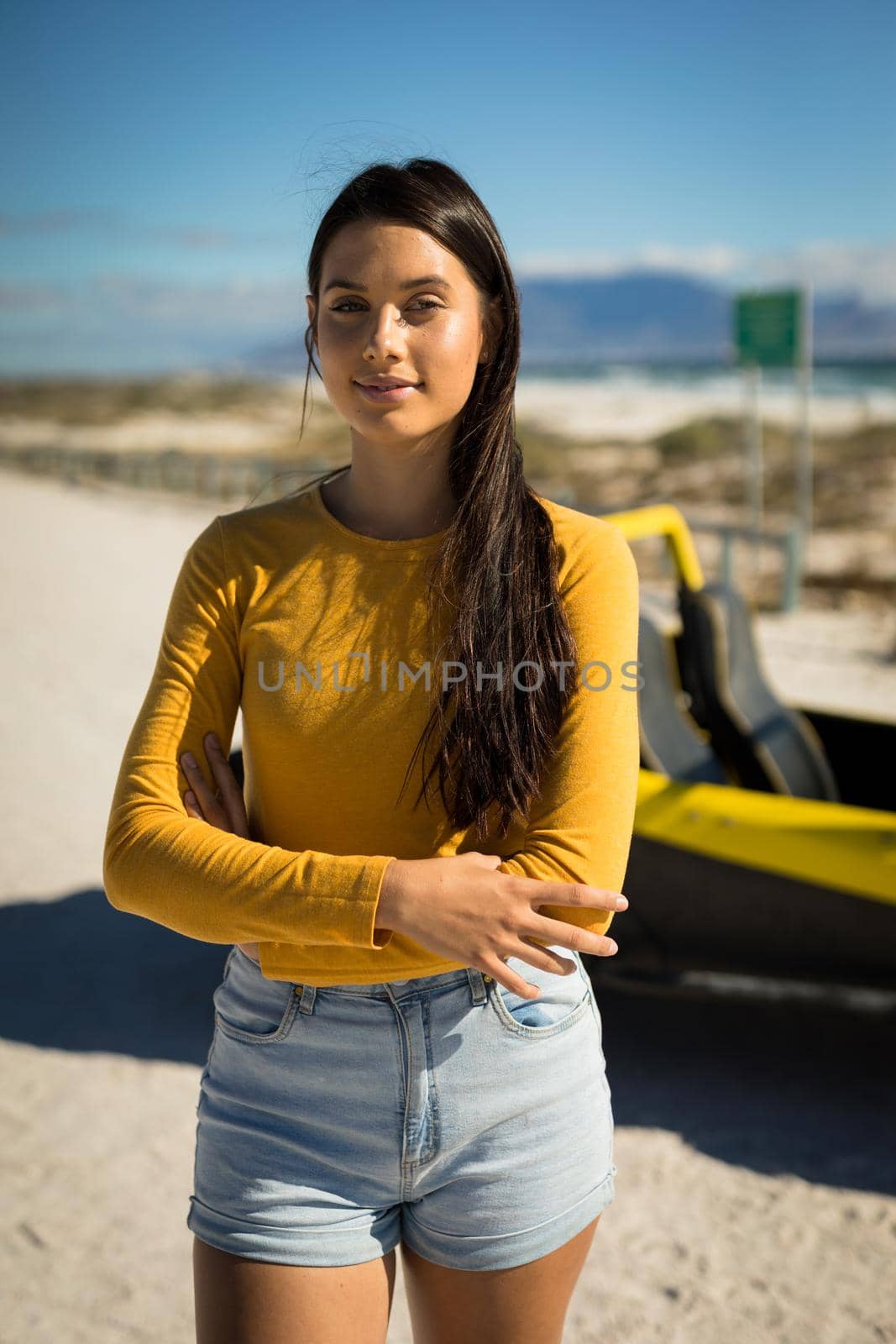 Portrait of happy caucasian woman staying next to beach buggy by the sea looking to camera. beach break on summer holiday road trip.