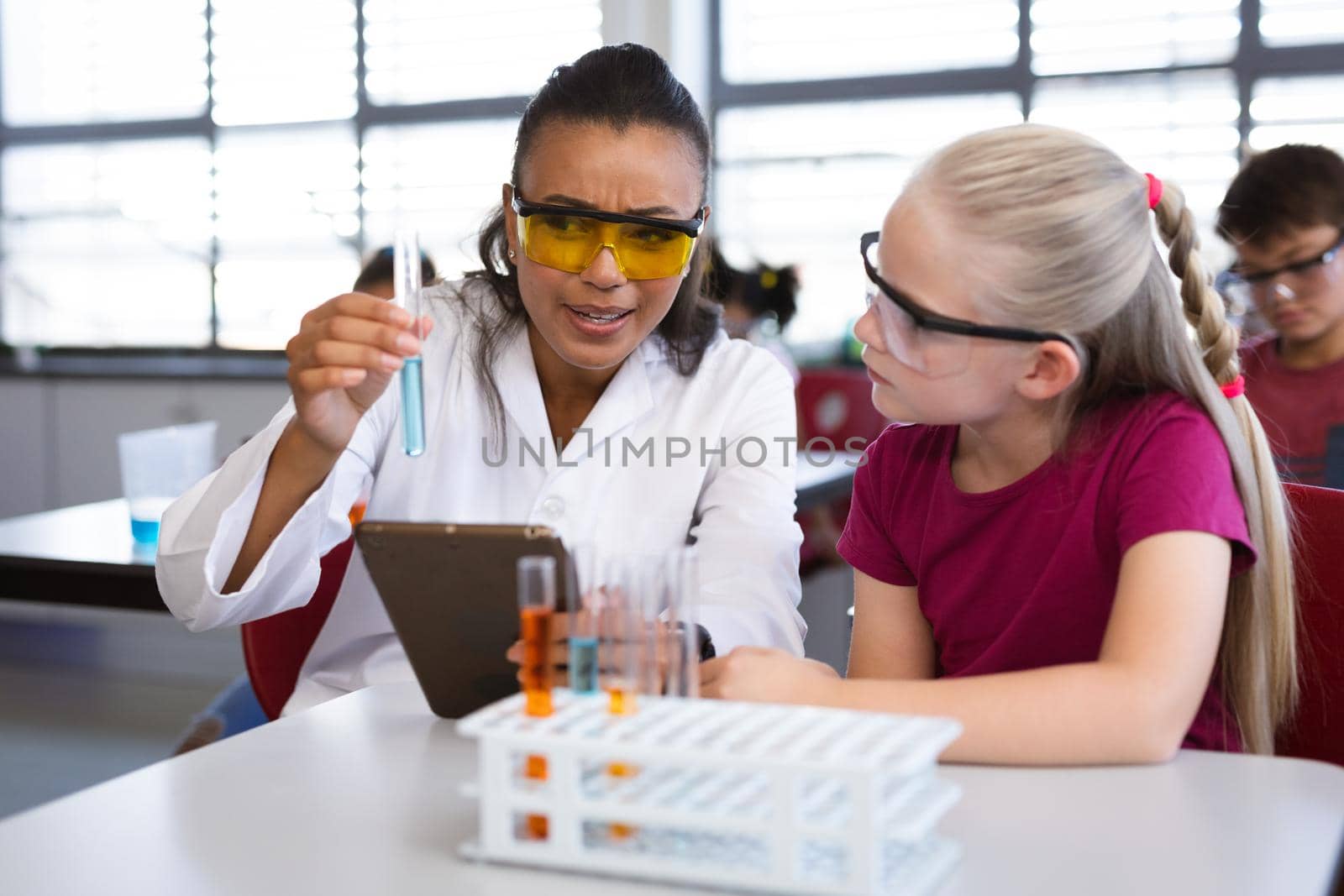 African american female teacher teaching chemistry to a girl during science class at laboratory. school and education concept